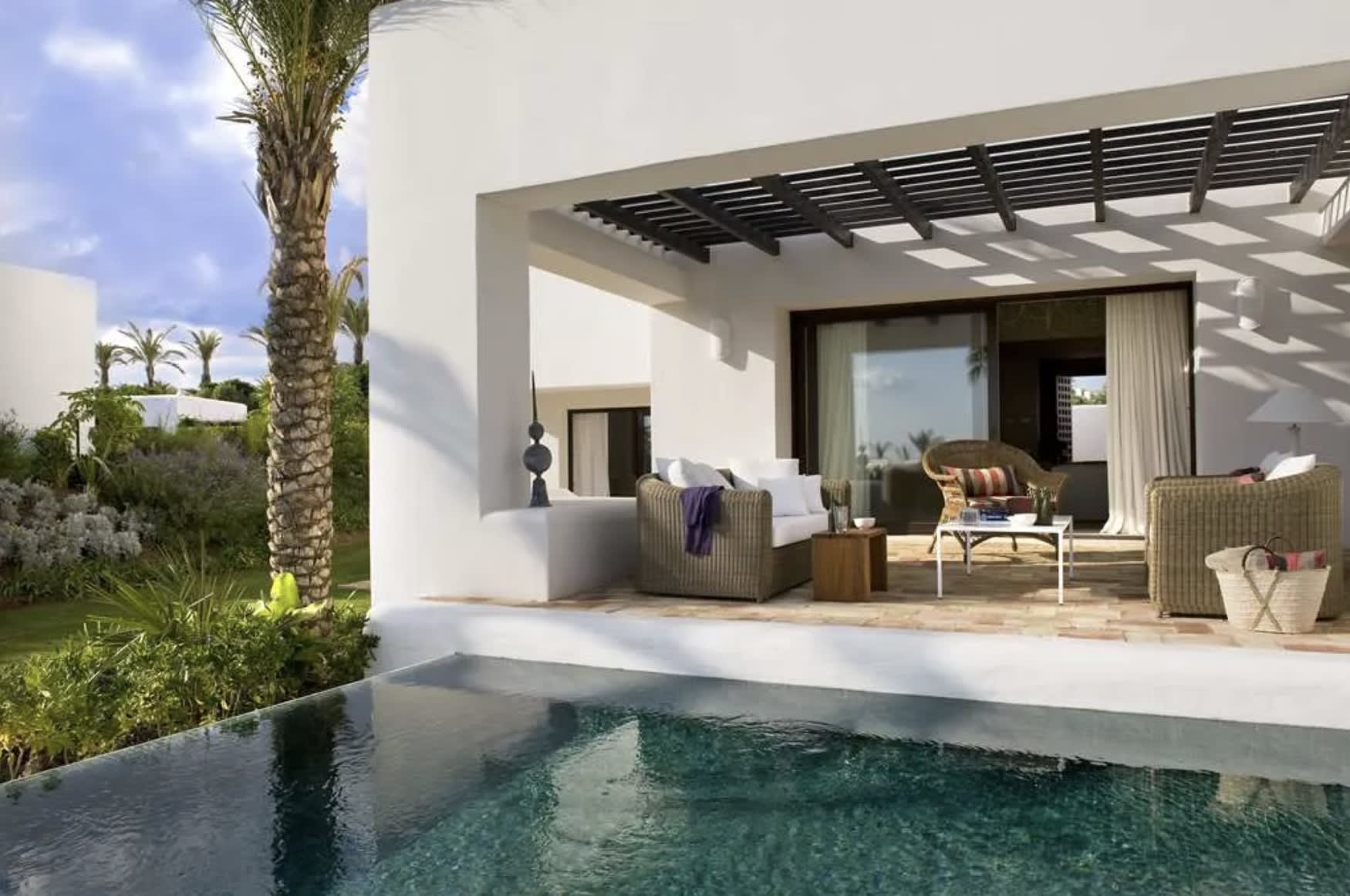 pool and palm tree next to a white terrace with furniture