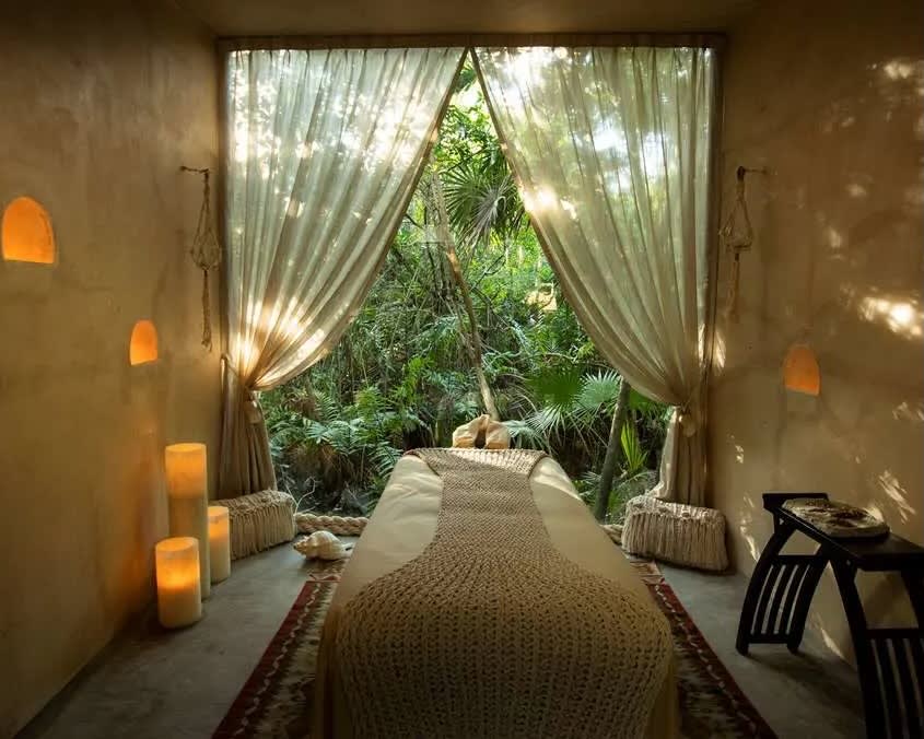 A massage table with tan sheets and candles hanging on the walls overlooking the jungle