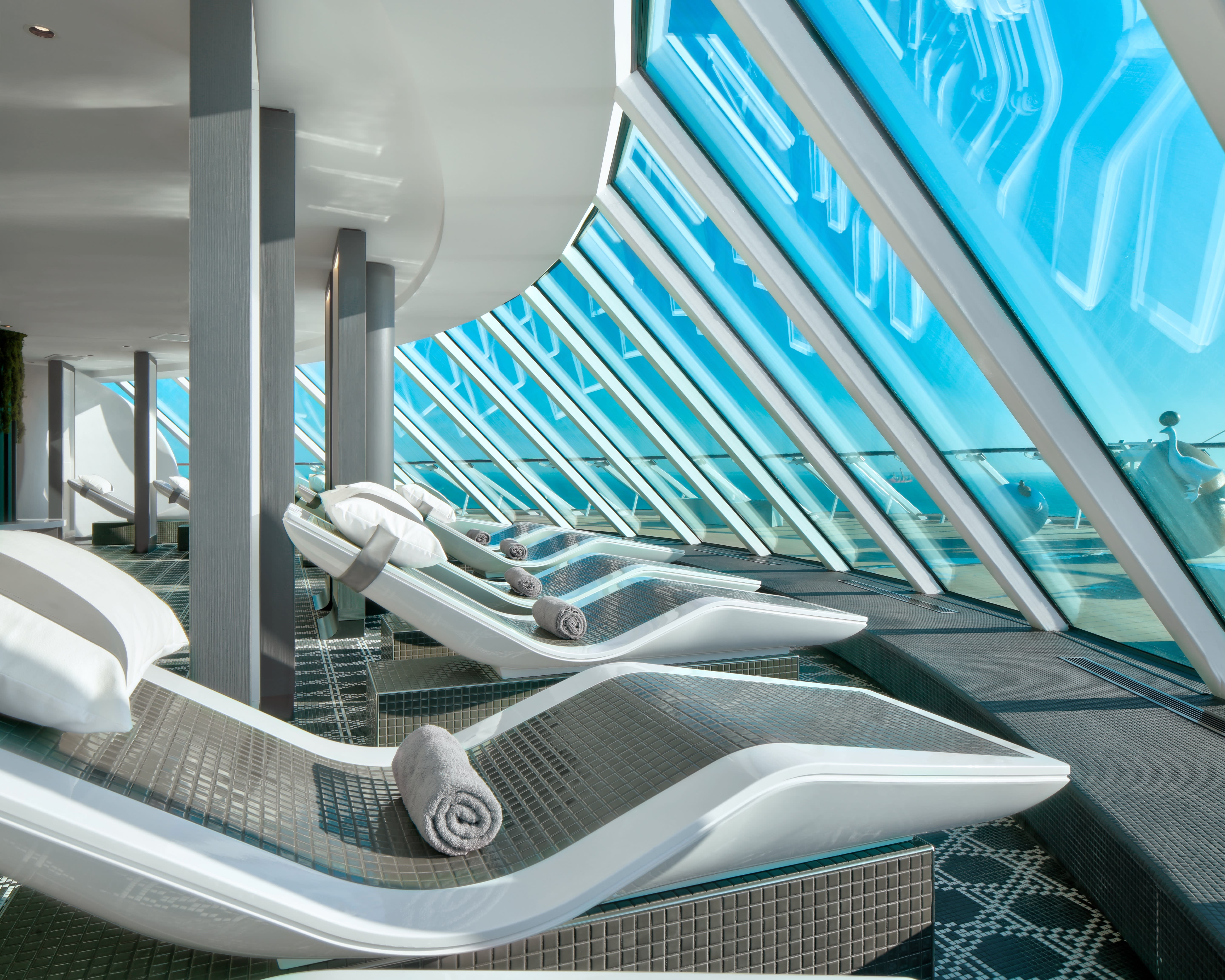 white and gray thermal spa with stone lounge chairs looking out windows during day