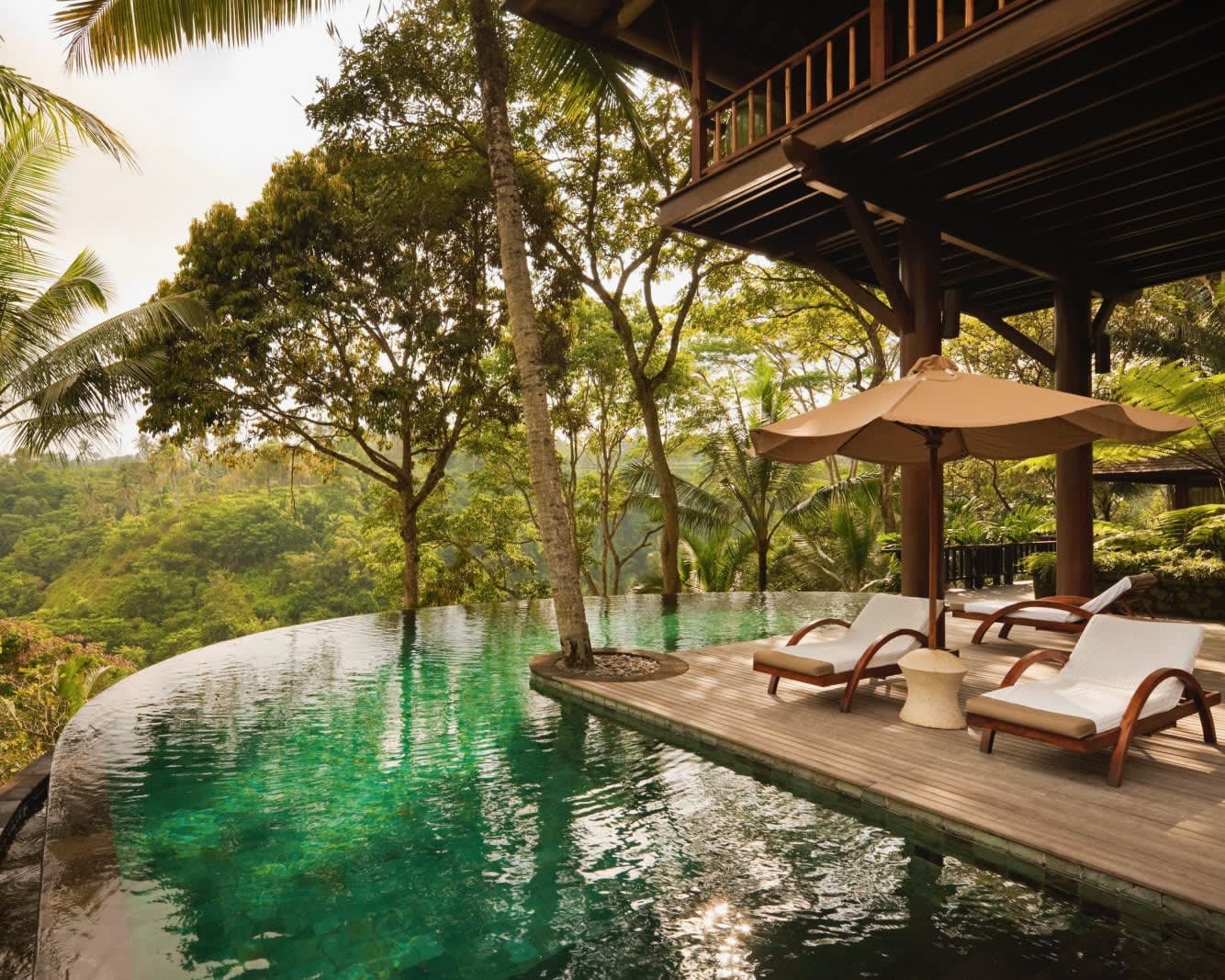 white lounge chairs next to a private pool under a wood cabin overlooking a green jungle during day
