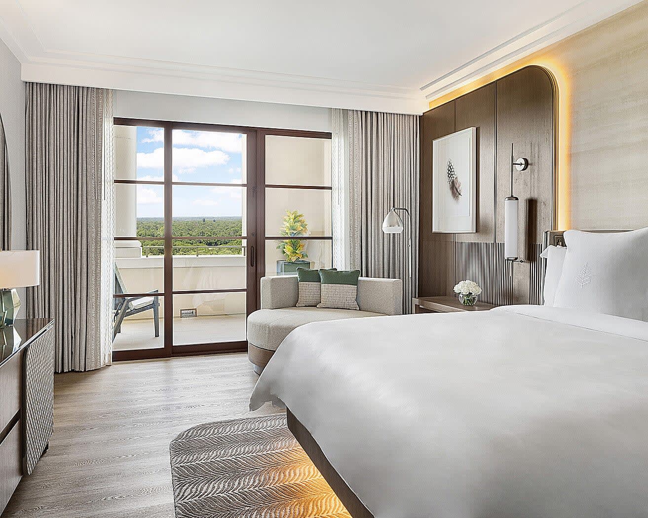 modern room with white bed, circular side lounge chair, dark wood wall panel, and glass doors leading to a balcony during day