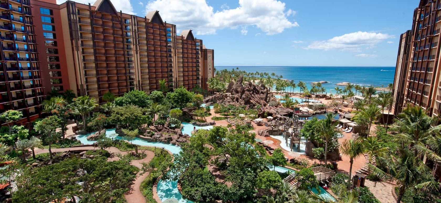 resort view of landscaped pools with tall brown hotel buildings next to the ocean during day