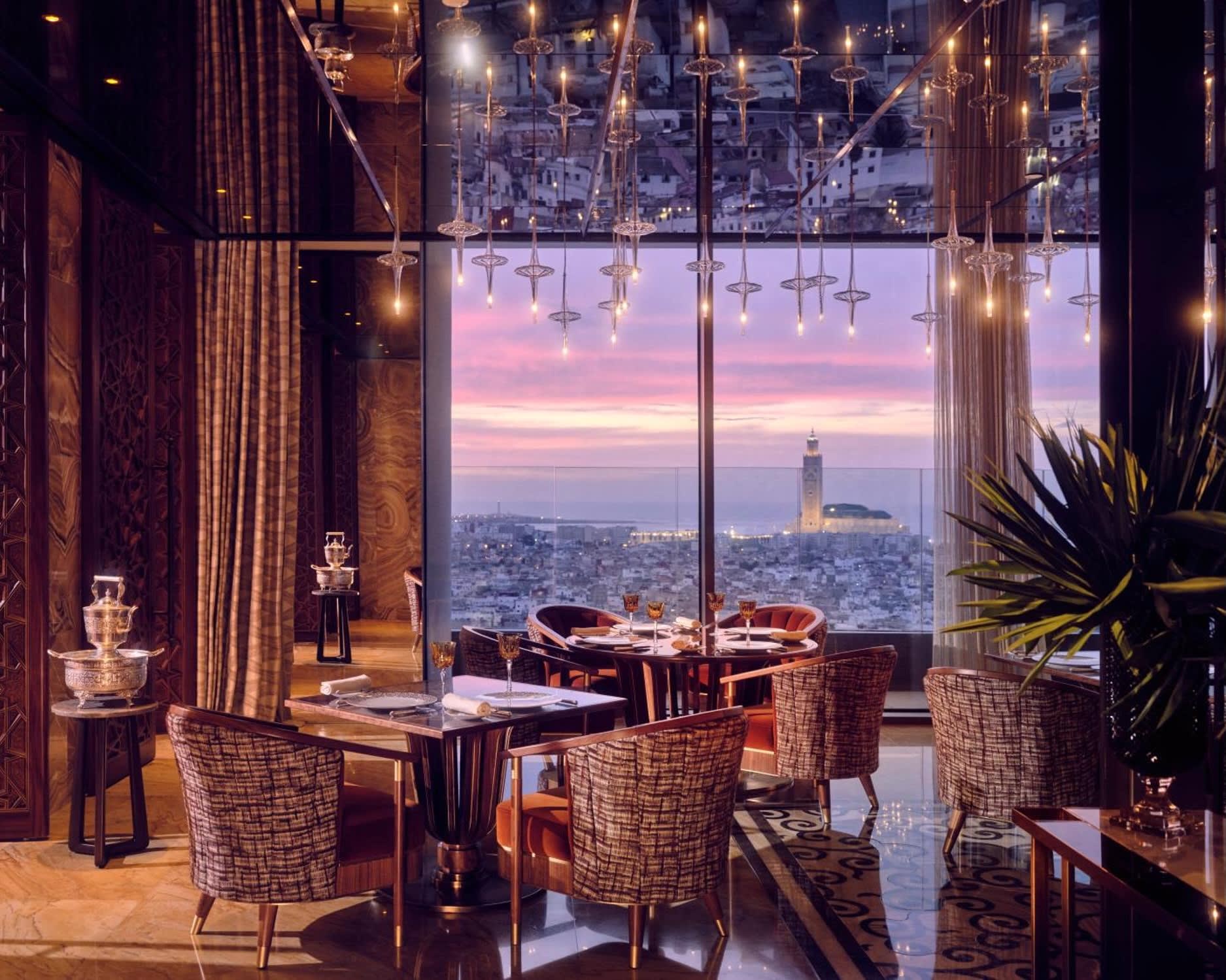 upscale restaurant with tables and chairs under mirrored ceiling overlooking a city at dusk with tower in the distance