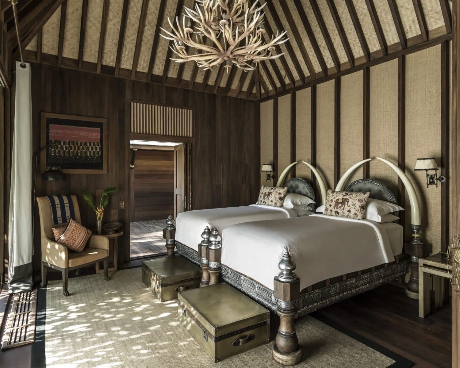 twin beds with elephant tusk bed frames, a wooden chair, and tusk chandelier above the bed