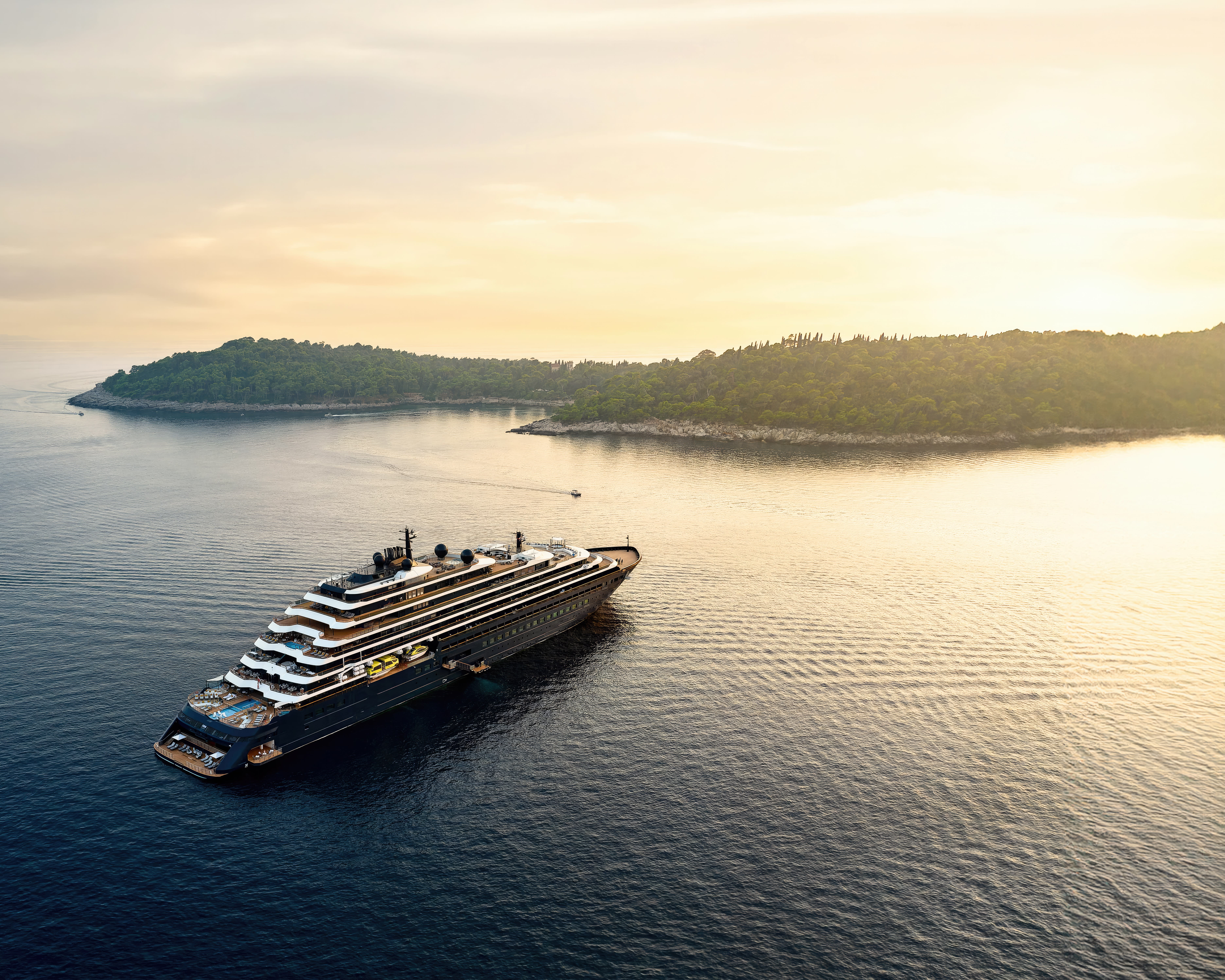 yacht style ship off a tree covered island with the sun setting on the horizon