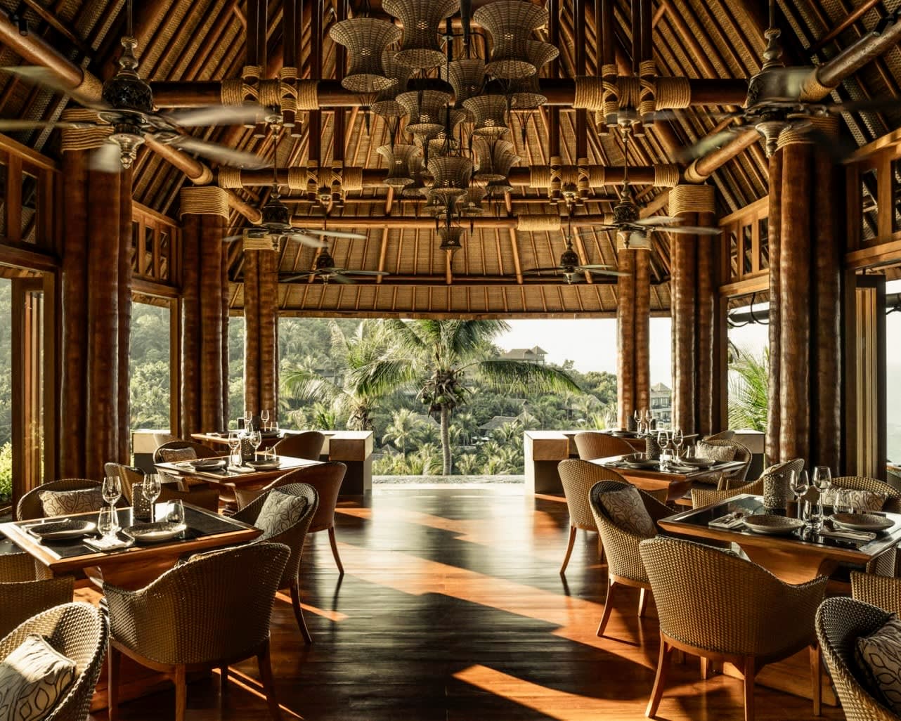 vaulted wood ceilings with tables and chairs off to each side along open windows overlooking tropical green trees