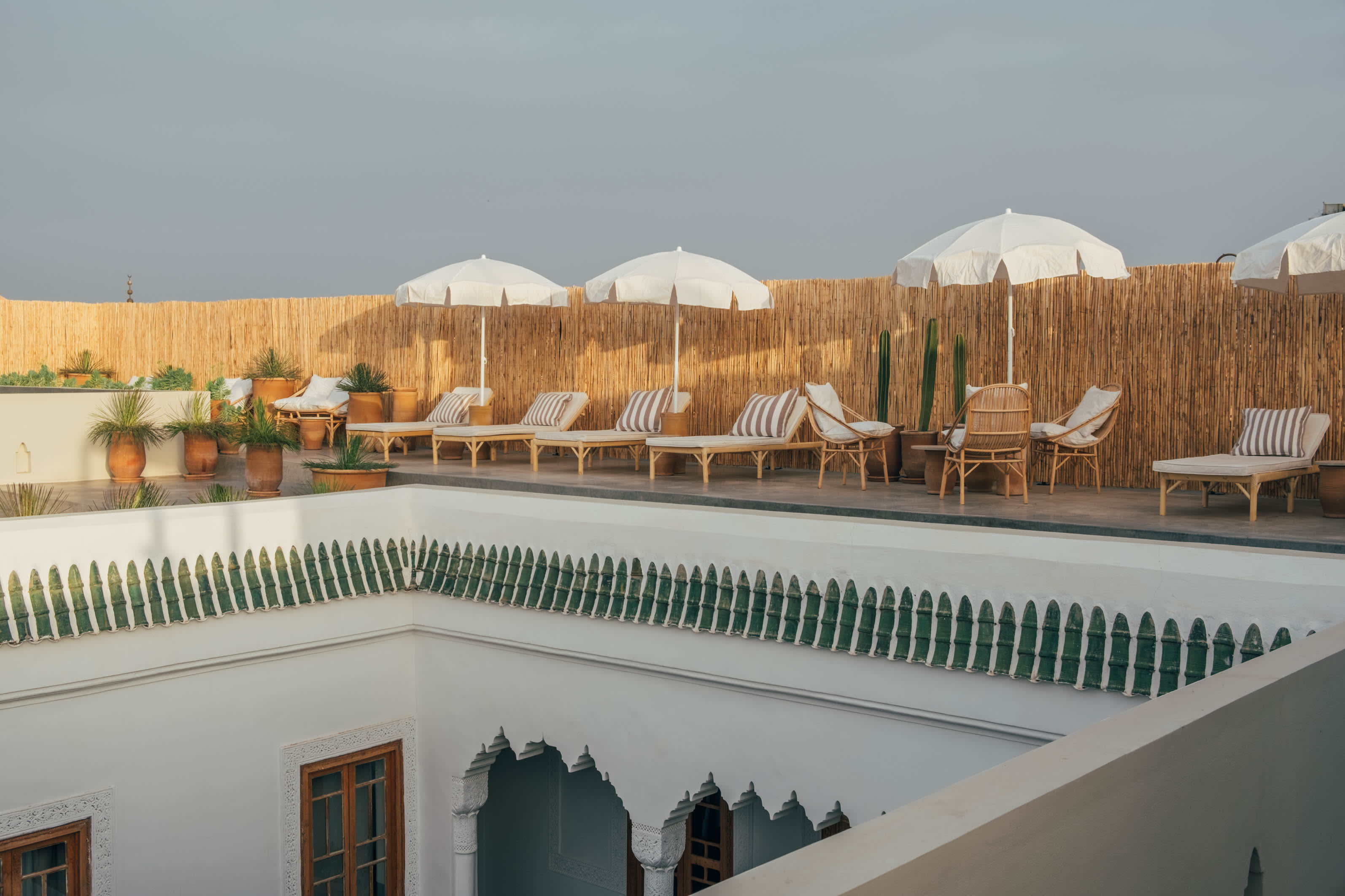 Rooftop terrace at Nobu Marrakech with woven lanterns, timber pergola beams, low lounge seating, and hanging rattan chairs, set against golden-hour views of the Medina and Koutoubia Mosque in the distance.