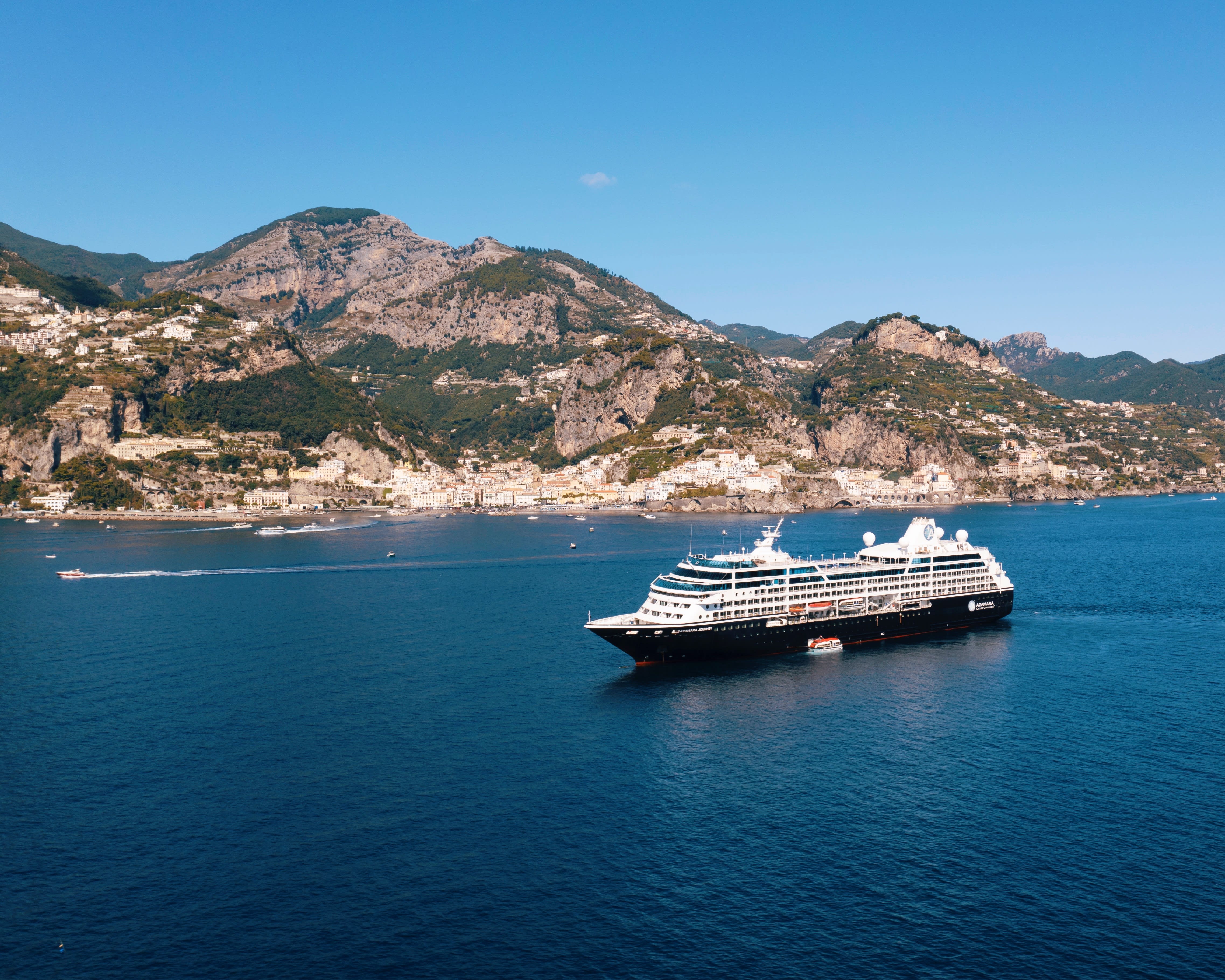 Cruise ship in turquoise waters off a green rocky hillside village