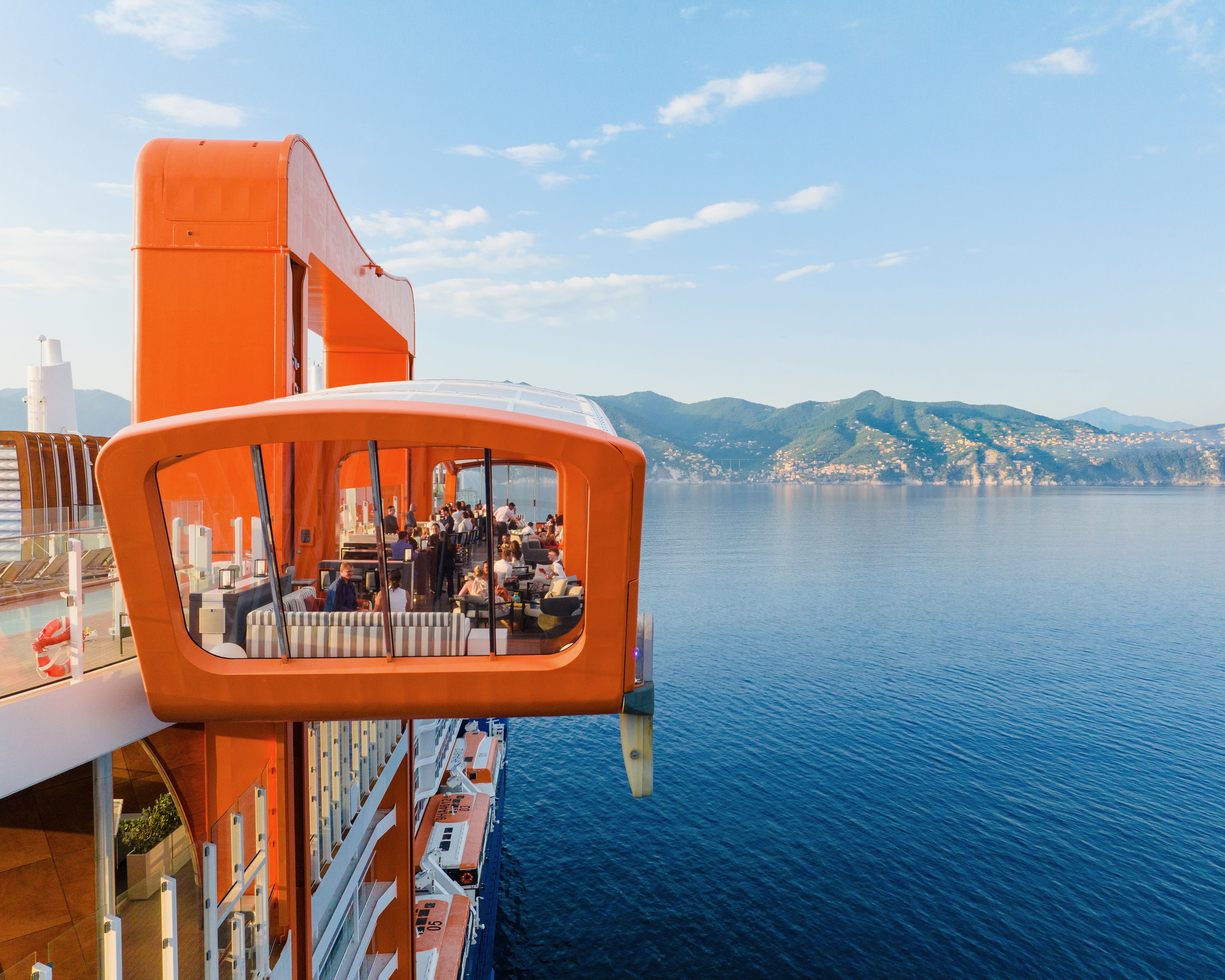 an orange restaurant deck off the side of a cruise ship off a hilly coastline during day