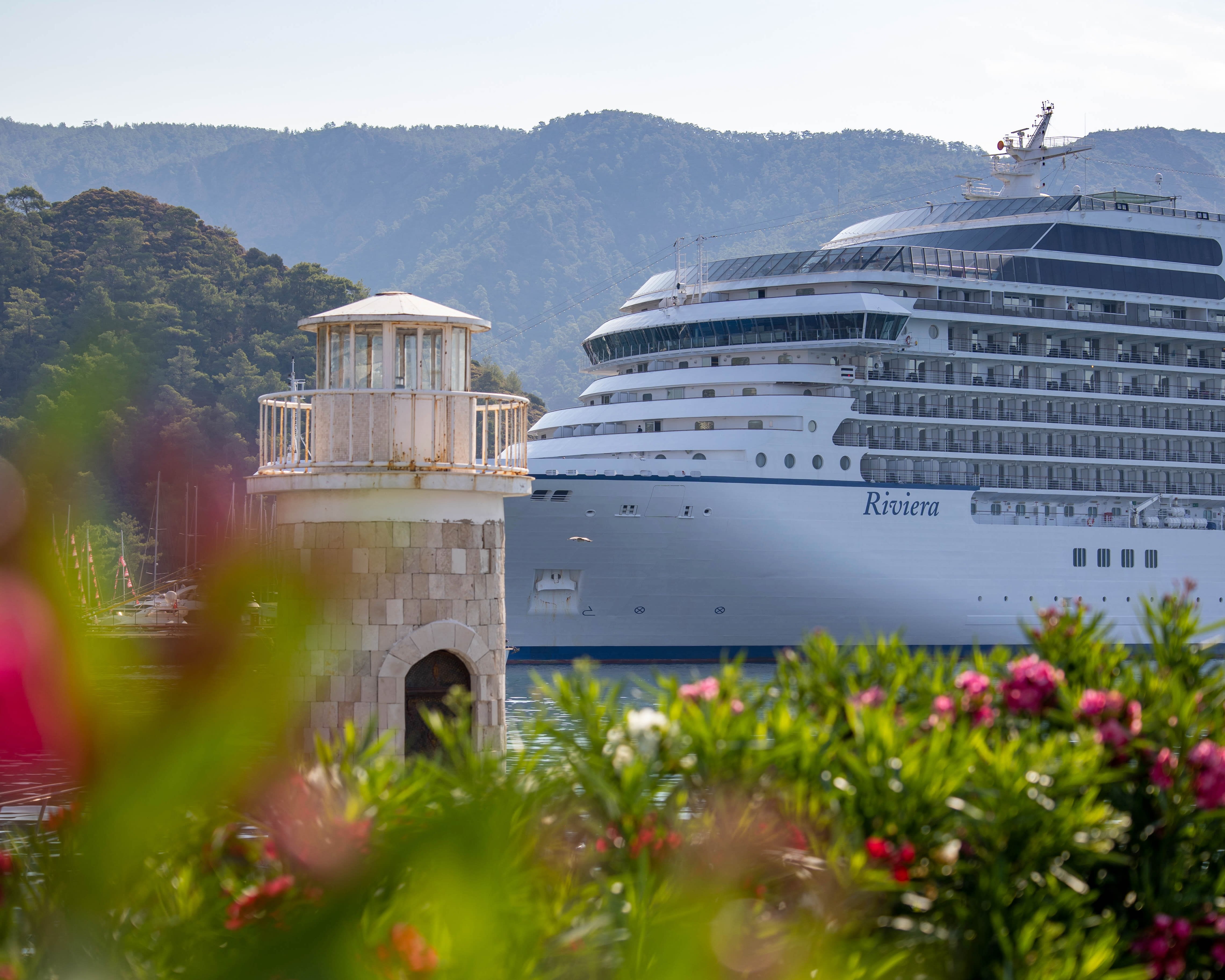 White cruise ship docked next to a small lighthouse and hillside