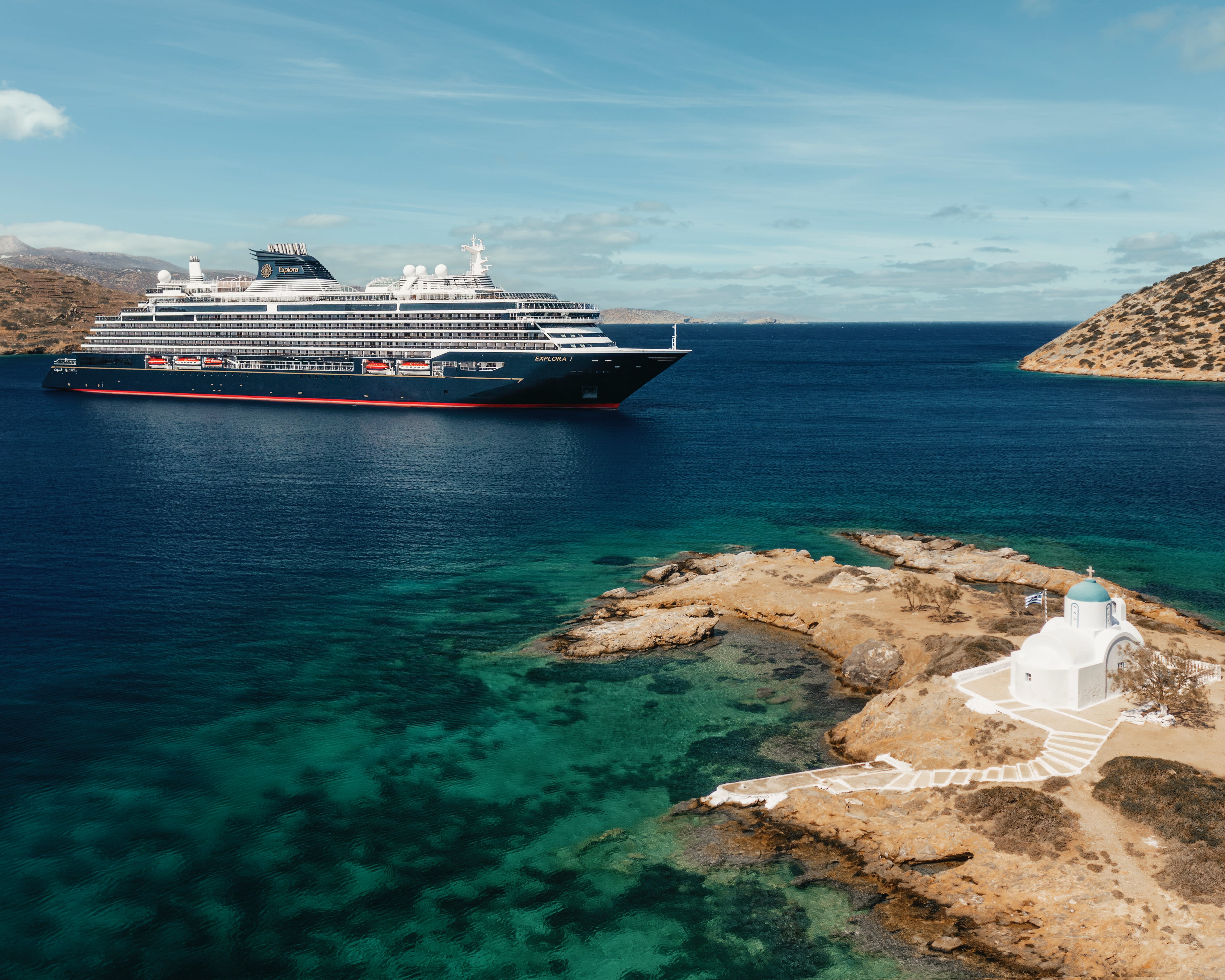 small cruise ship in turquoise water off a tan coast with white building and blue roof