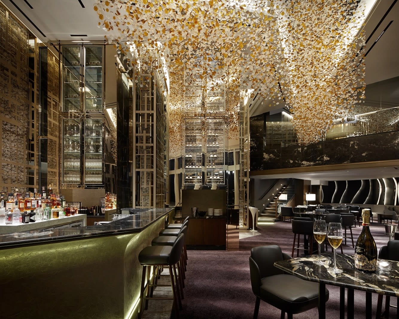 gold glass chandelier above a green bar with alcohol bottles and stools