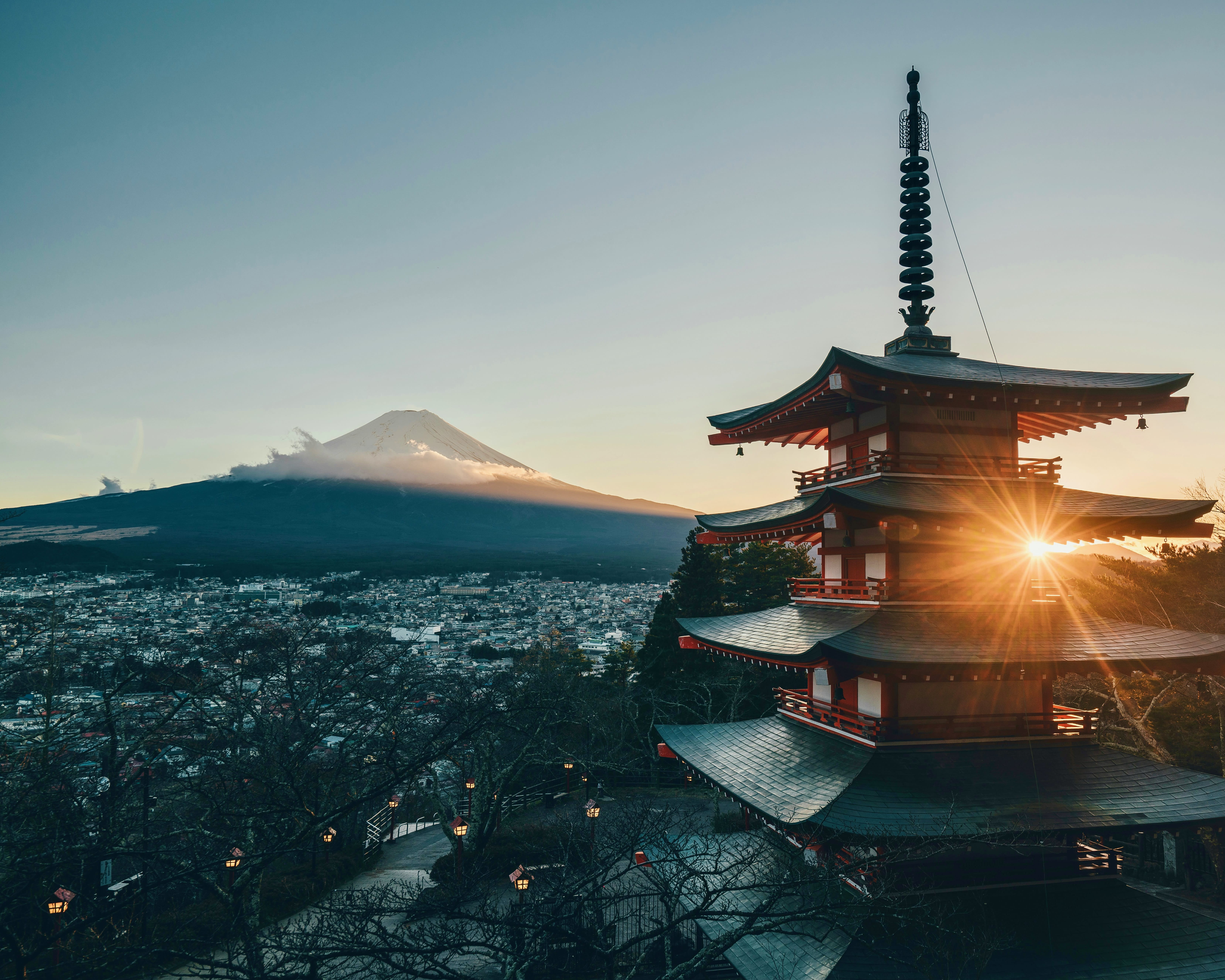 sun setting behind a tall pagoda with snow-capped mountain in the distance