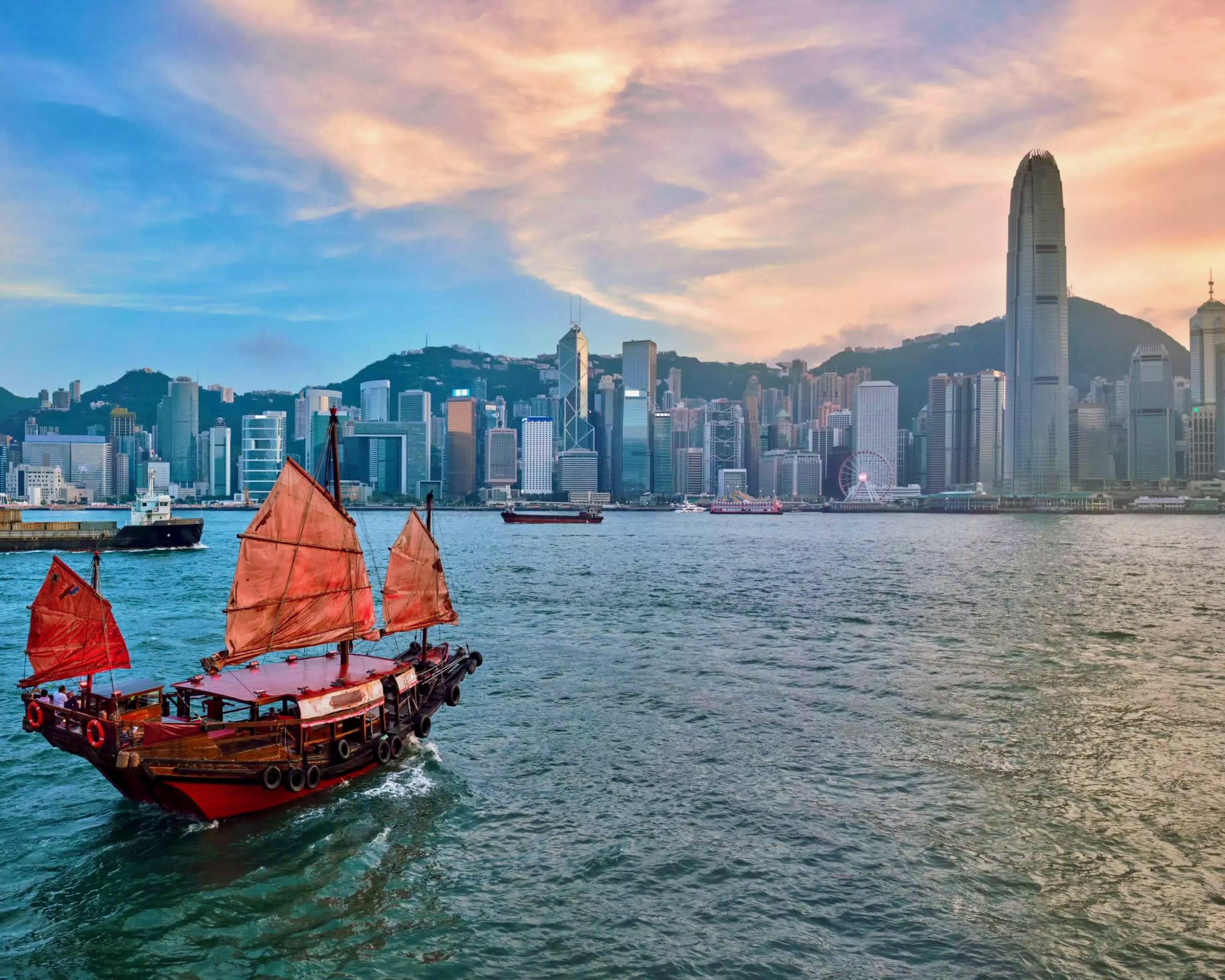 traditional dhow boat in a harbor with skyscrapers along the shore at dusk