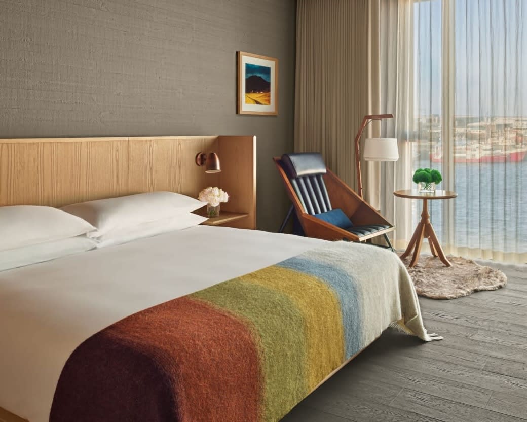 hotel room with grey wall, wood furniture, white bed linens and multicolor blanket