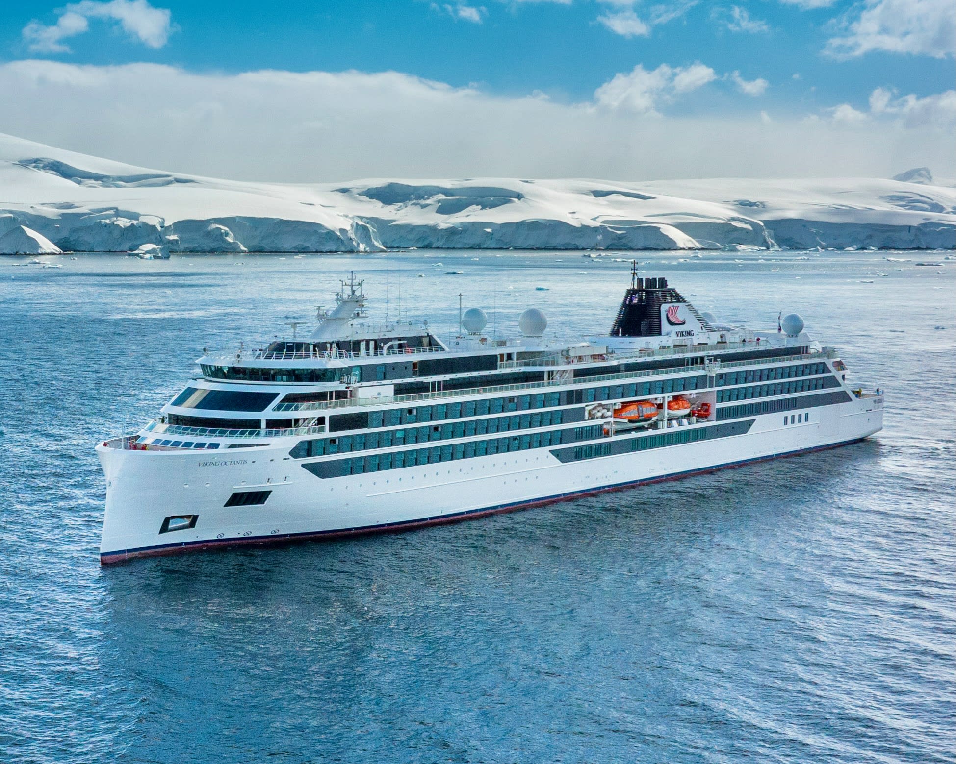 white expedition cruise ship at sea with snow covered cliffs during day in the background