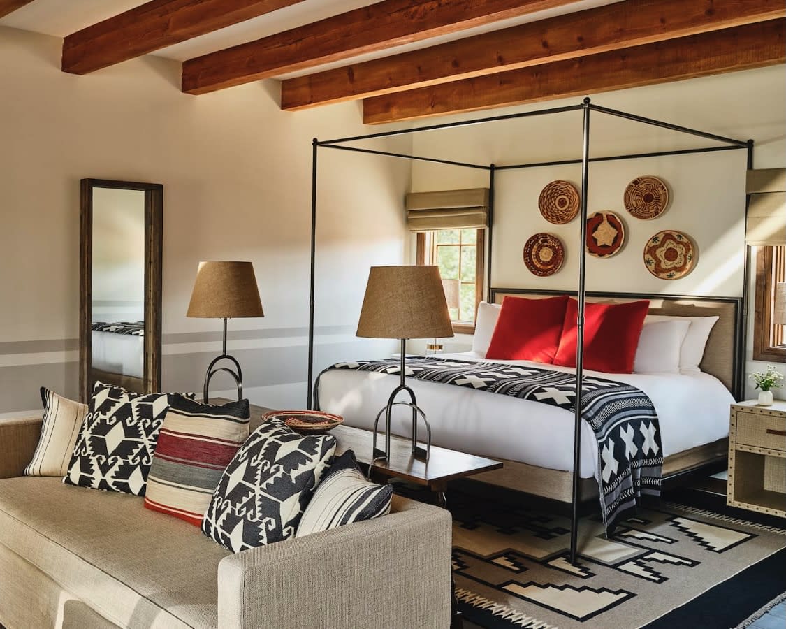 cream sofa in front of black metal four poster bed, black and white patterned accents and red pillows with wood beam ceiling