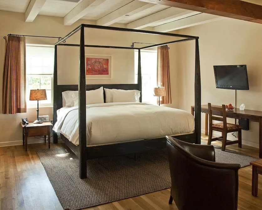 black four poster bed with white linens on a wood floor with grey rug and white wood beam ceiling