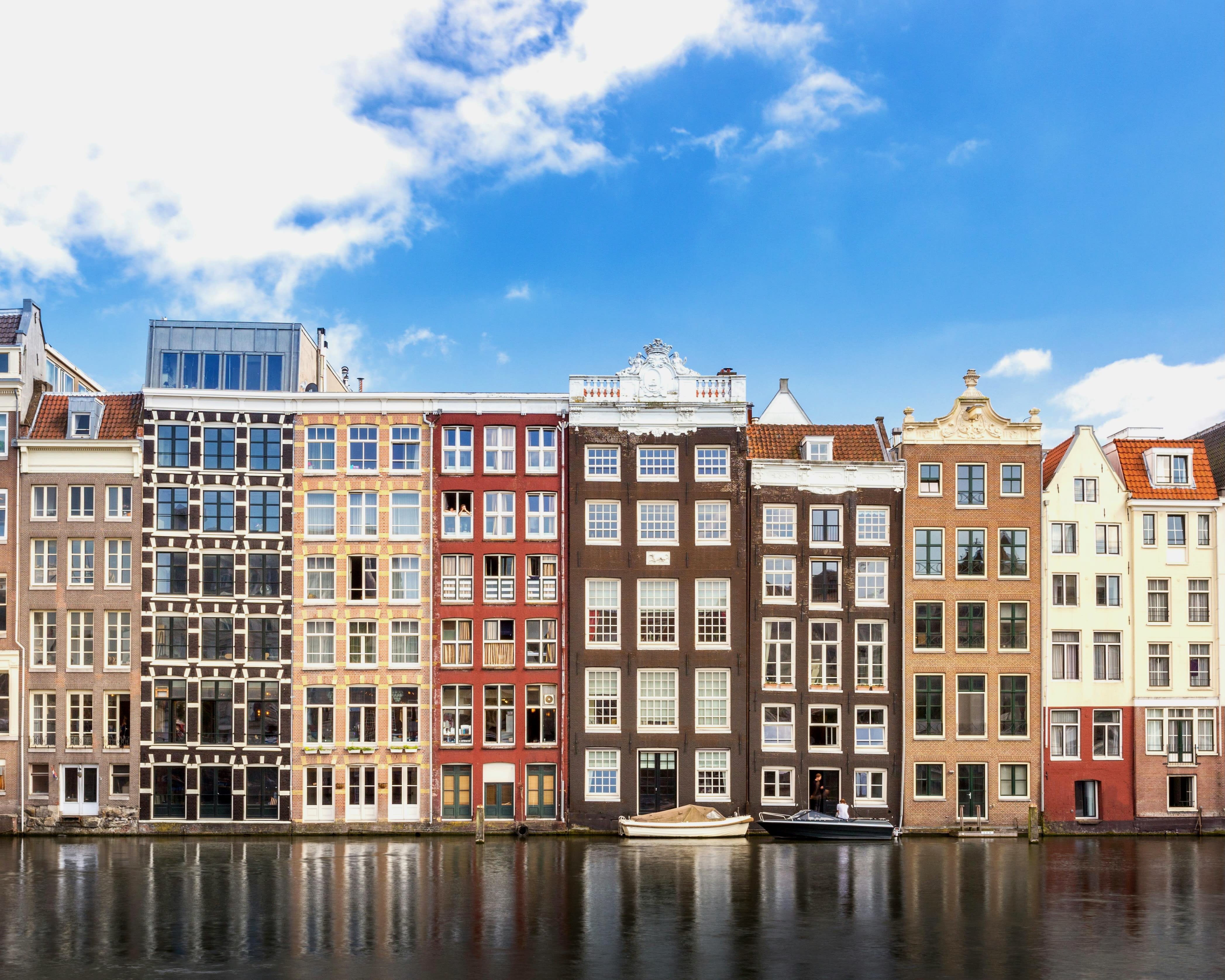 tall thin colorful buildings along a canal with boats in it and blue skies