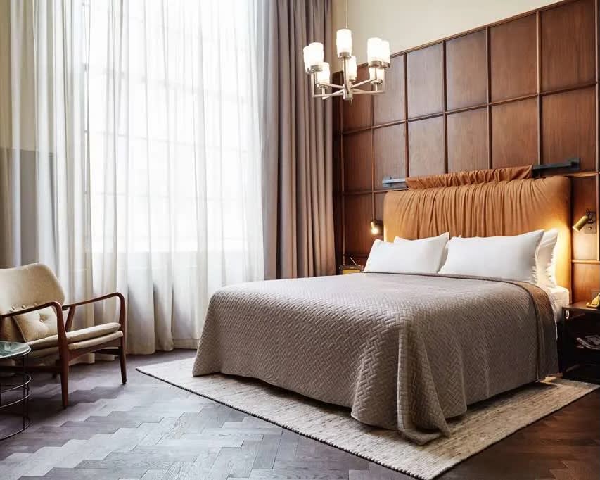 grey covered bed with tan wood wall and chandelier