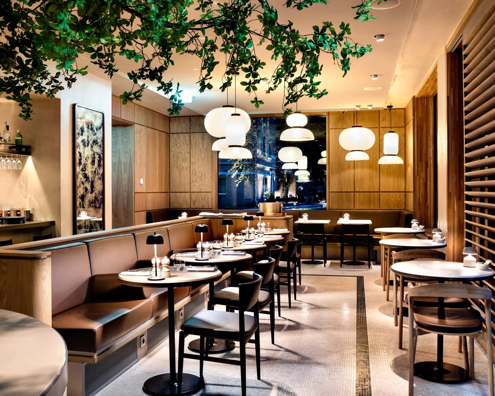 restaurant tables and chairs with earth tones under green leaves and lights