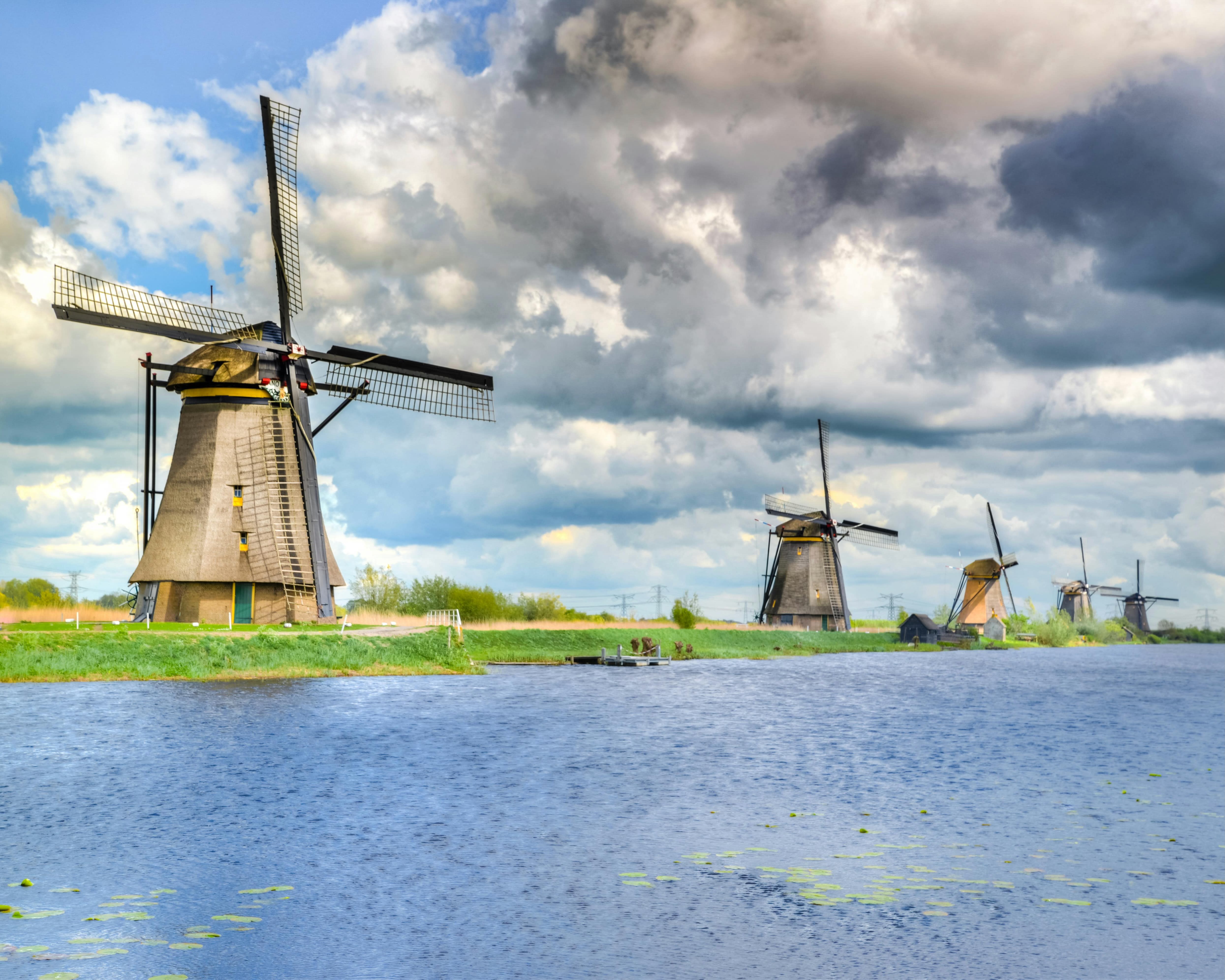 windmills next to water under cloudy skies during day