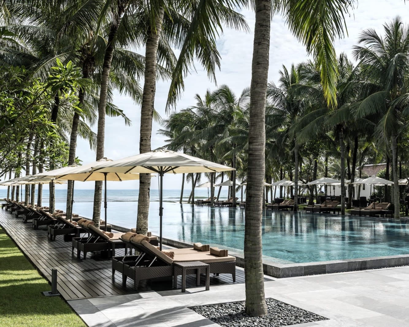 lounge chairs with umbrellas next to a pool under palm trees