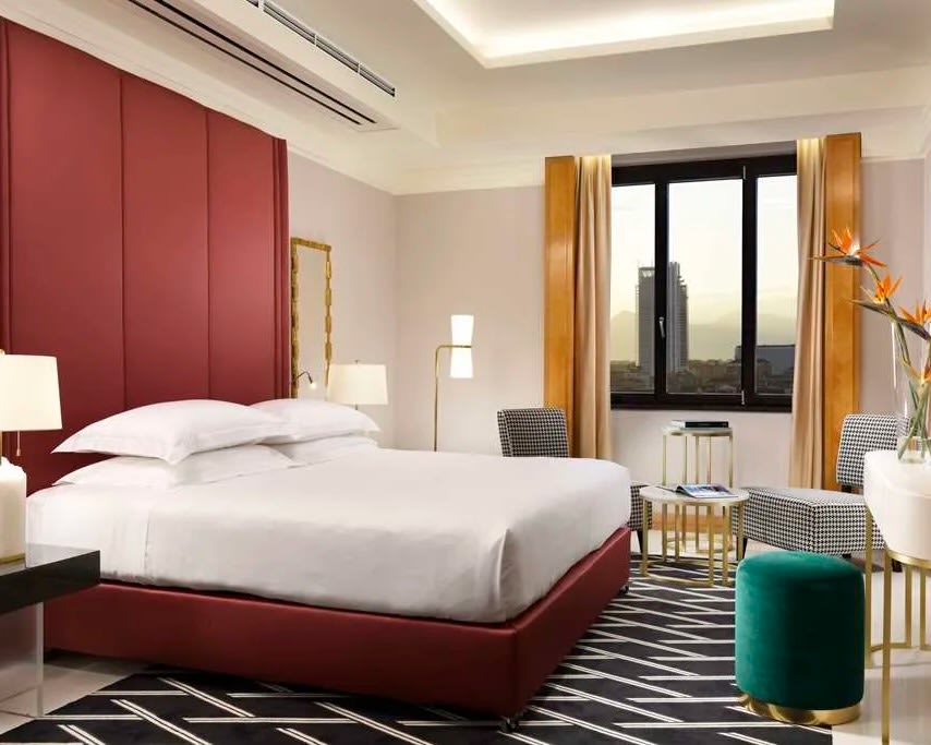 modern hotel room with red headboard, white bed sheets, green ottoman and gold curtains