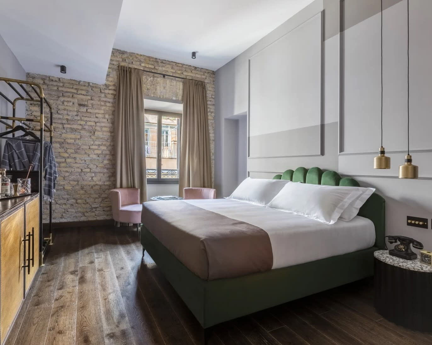 modern hotel room with green velvet bed frame, gold accent furniture, wood floors, and brick wall