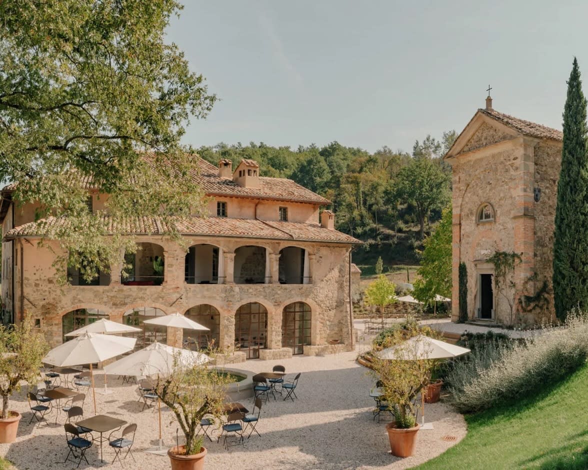 courtyard with tables and chairs and umbrellas next to rustic 12th century stone house buildings