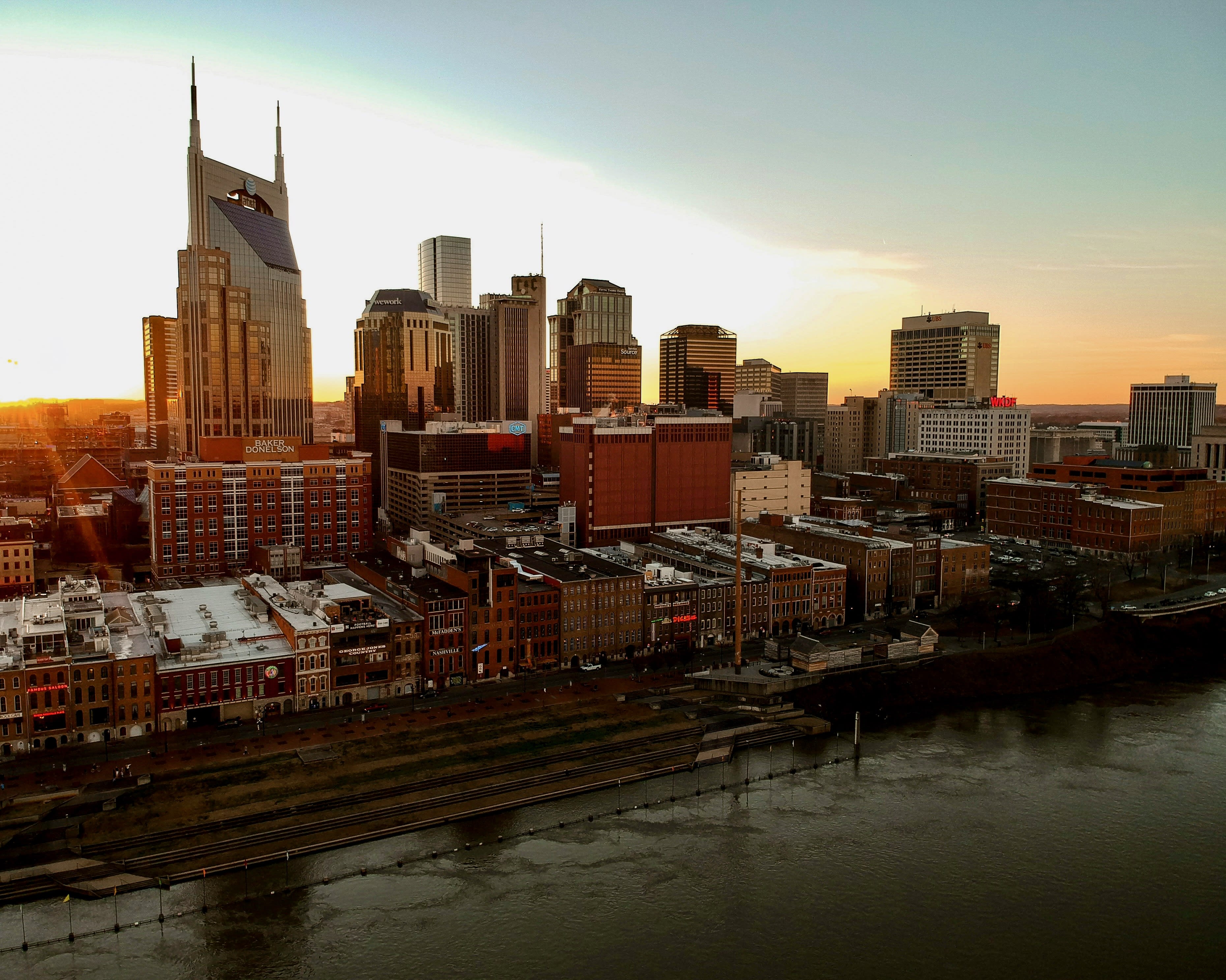 aerial cityscape of riverfront skyscrapers with the sun setting behind them