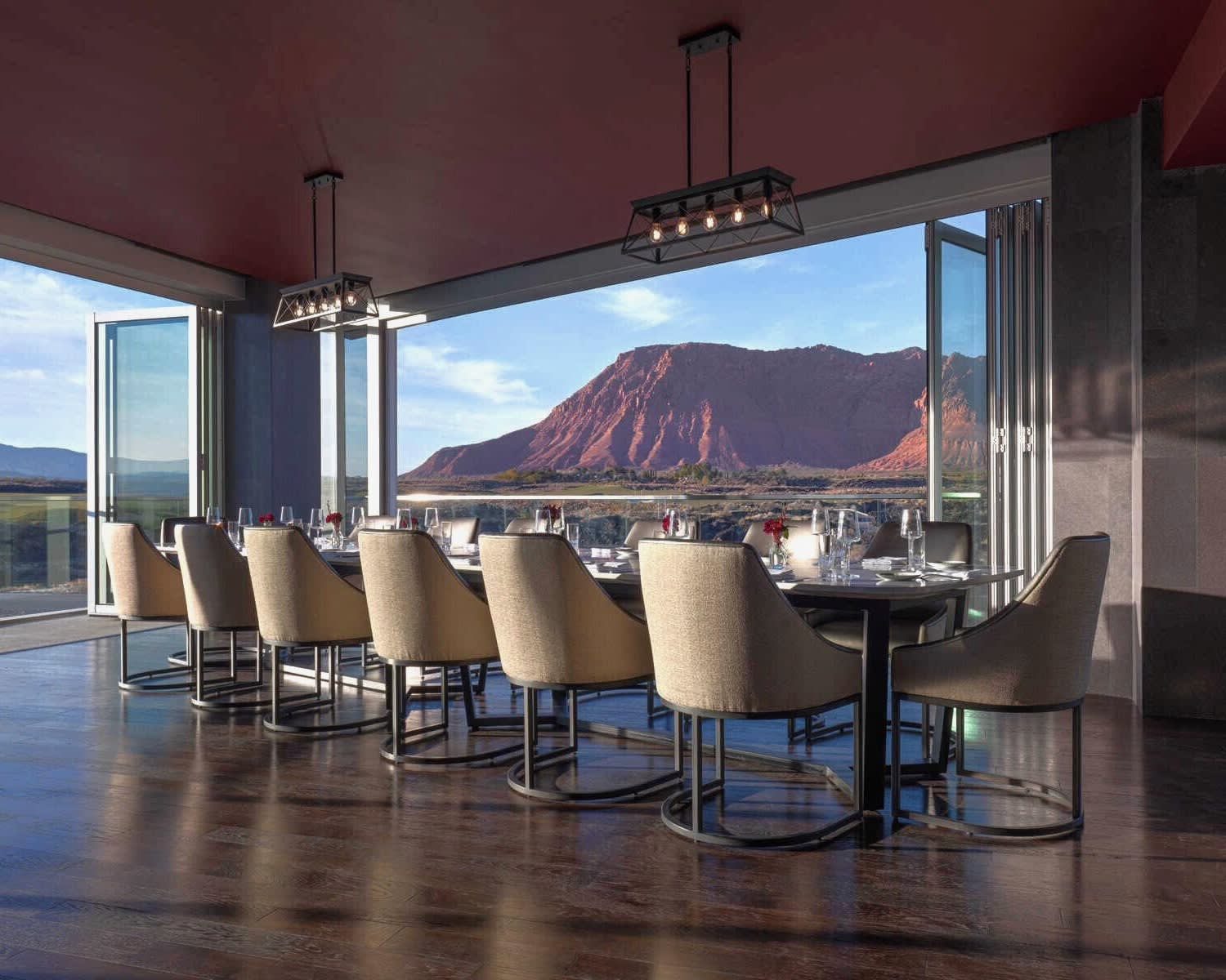group dining table with modern cream chairs around a long rectangle table with open windows to red mountains outside at dusk