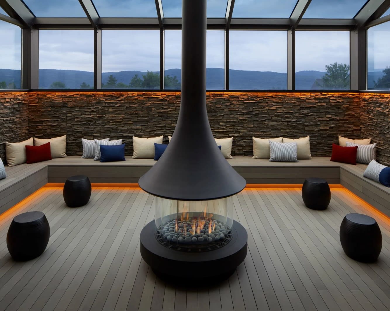 modern round black fireplace surrounded by stone benches, black stools, and colorful accent pillows