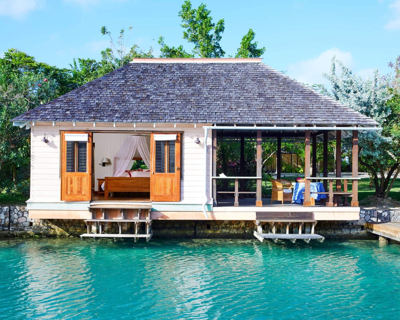 private white bungalow over turquoise water in front of green trees during day