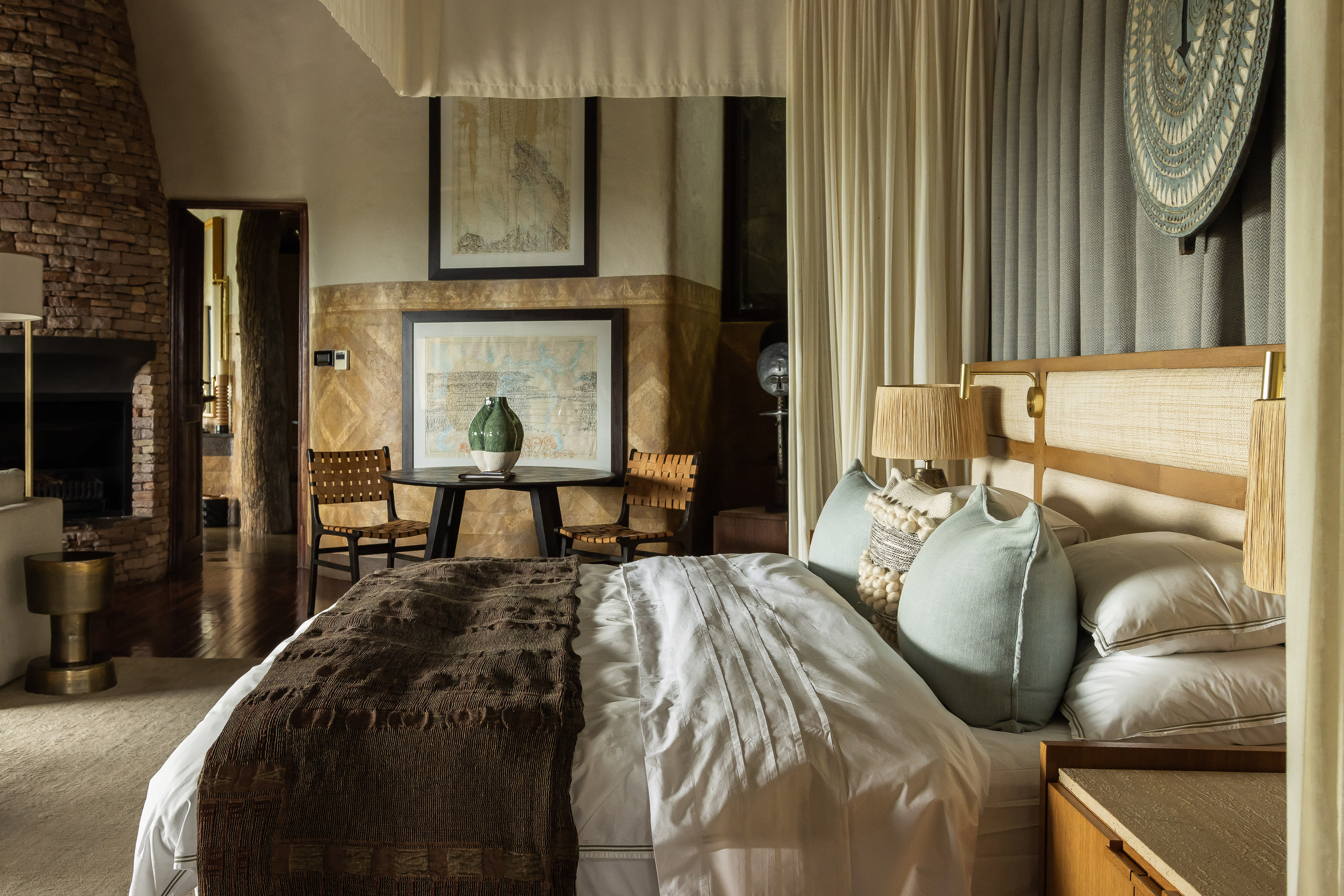 plush bed with curtain headboard, two simple chairs, and a brick fireplace
