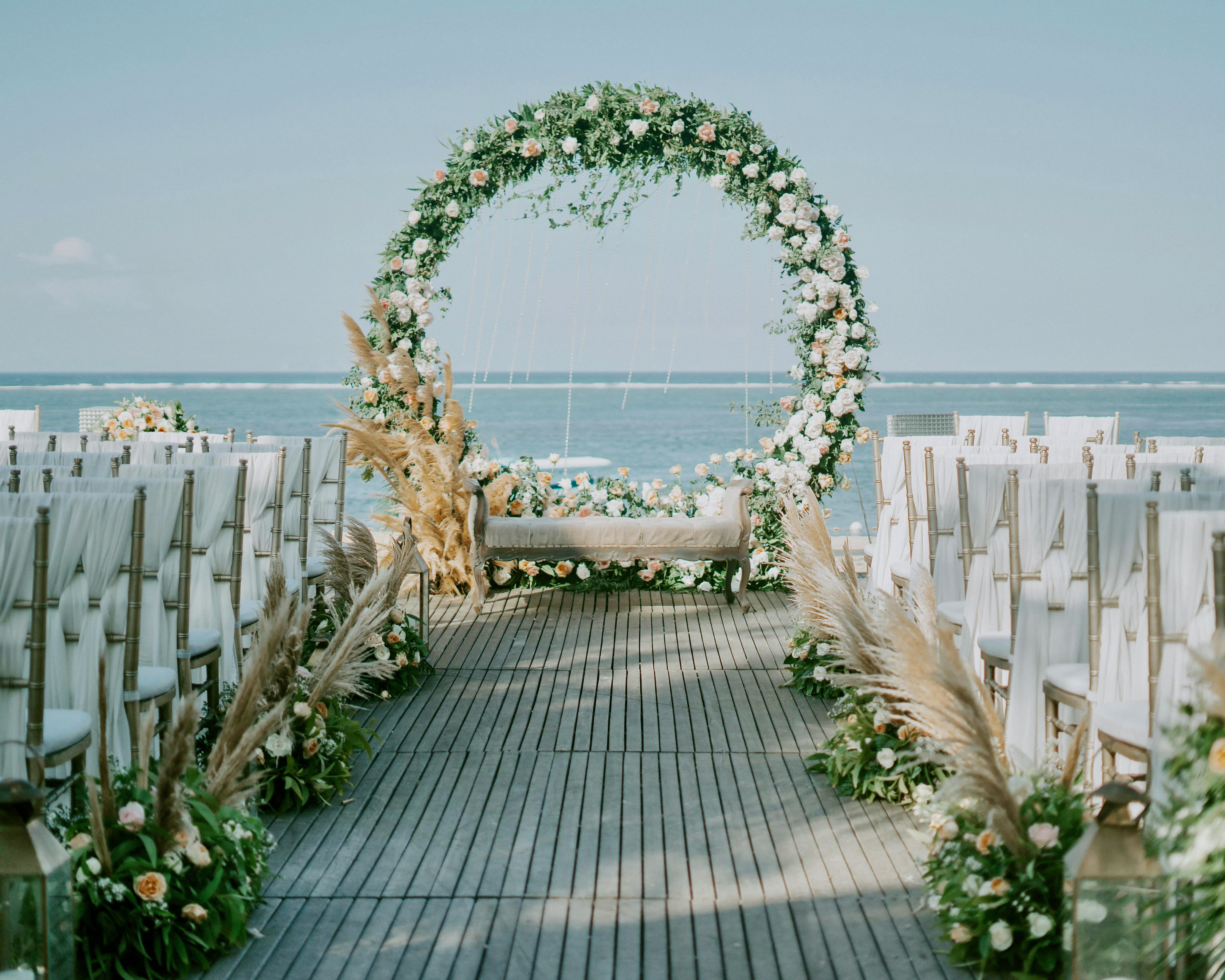 wood deck with white chairs facing a circular flower altar with the sea behind