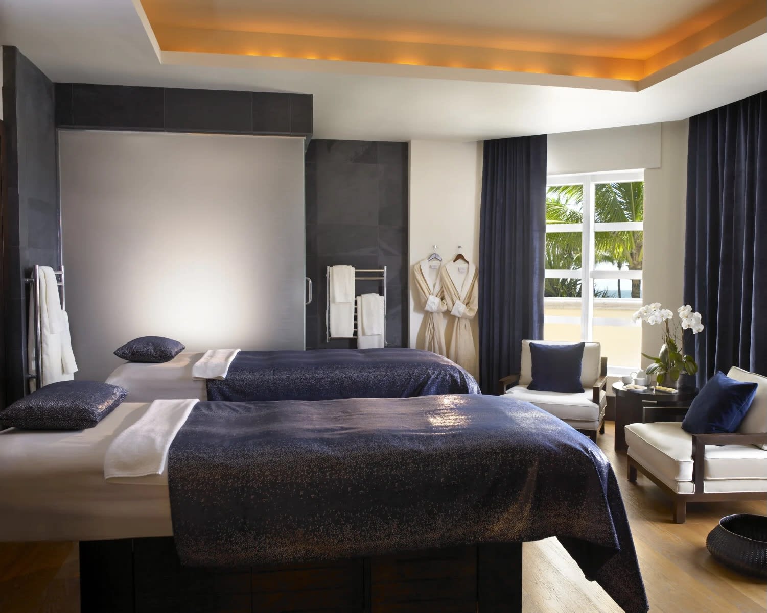 two massage tables side by side with white sheets and dark blue blanket and pillows