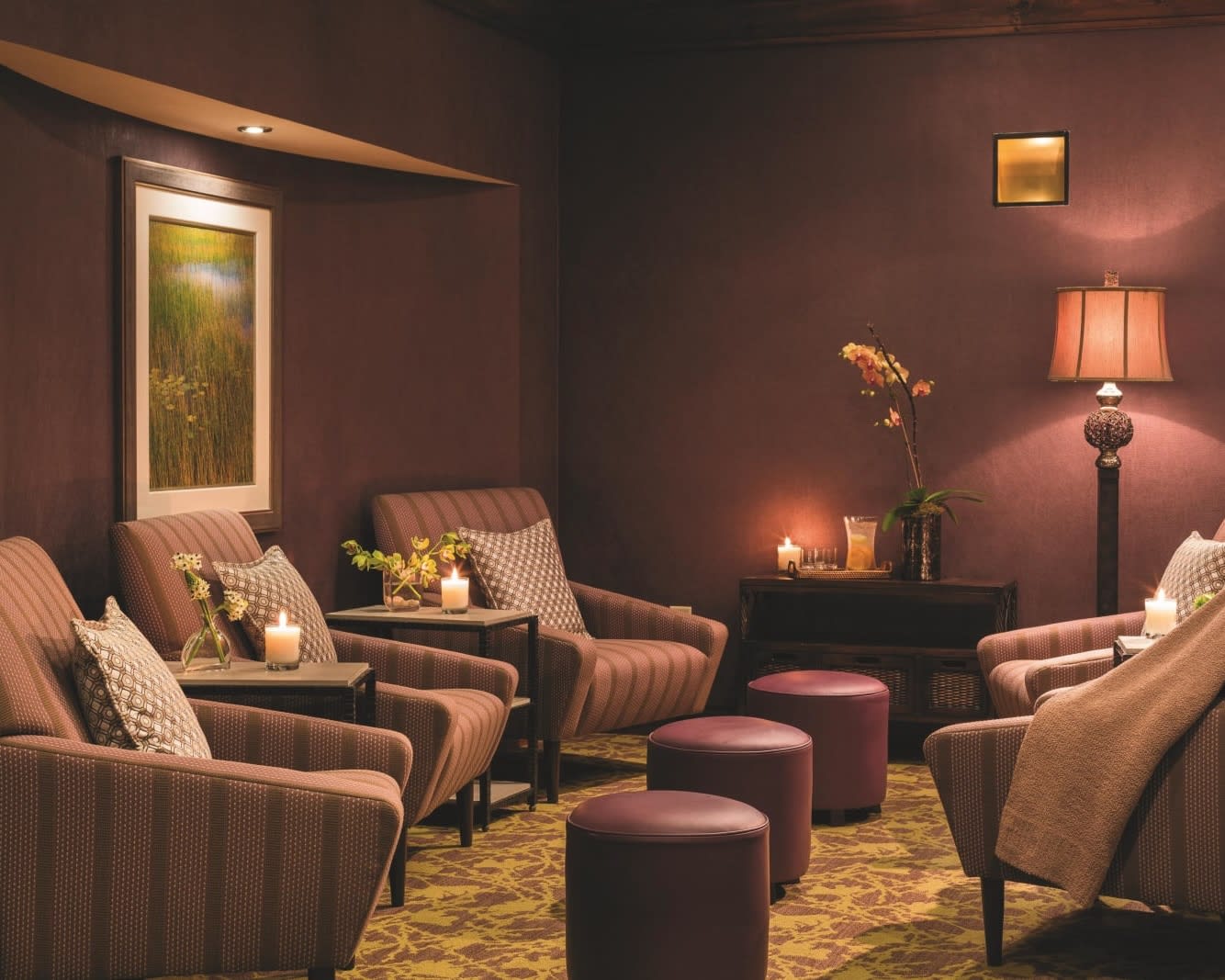 dark pink striped chairs around maroon ottomans with mauve colored walls in a relaxing setting
