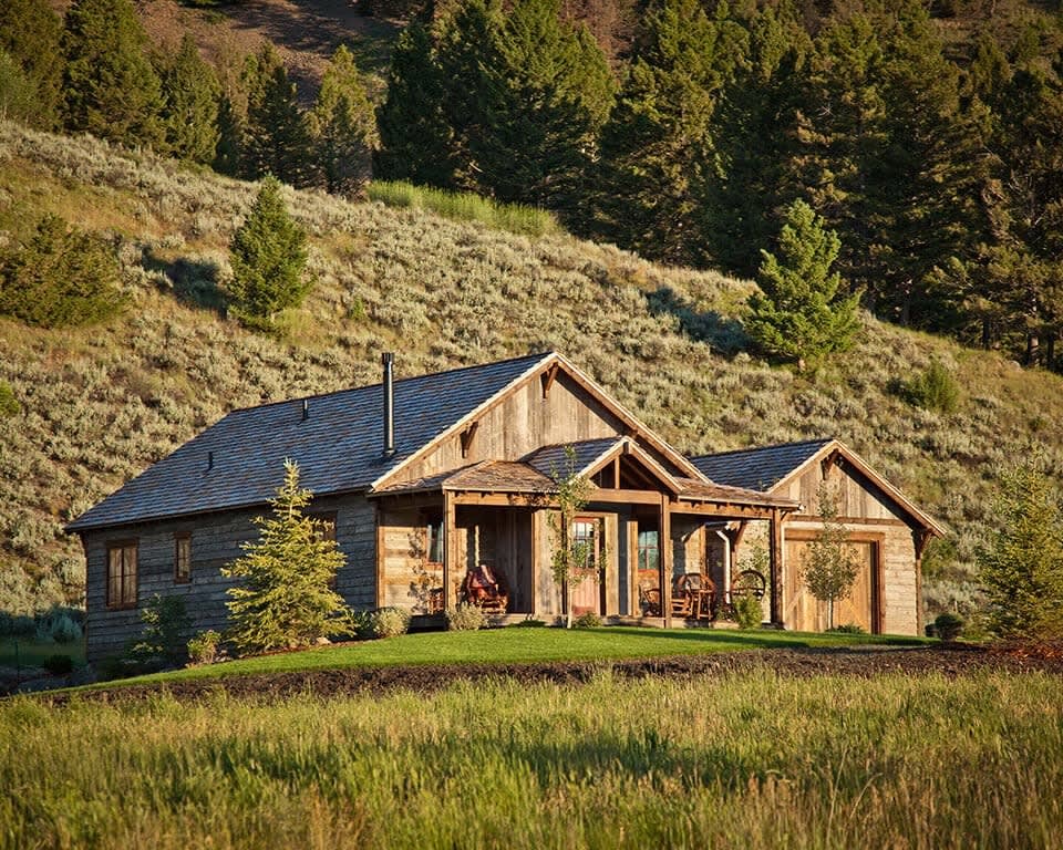 log cabin on a green hillside with trees behind it during day