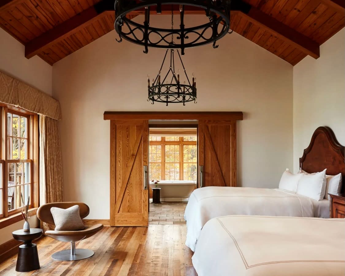 two white beds with dark wood headboard, wood floors and wood doors under black iron chandelier