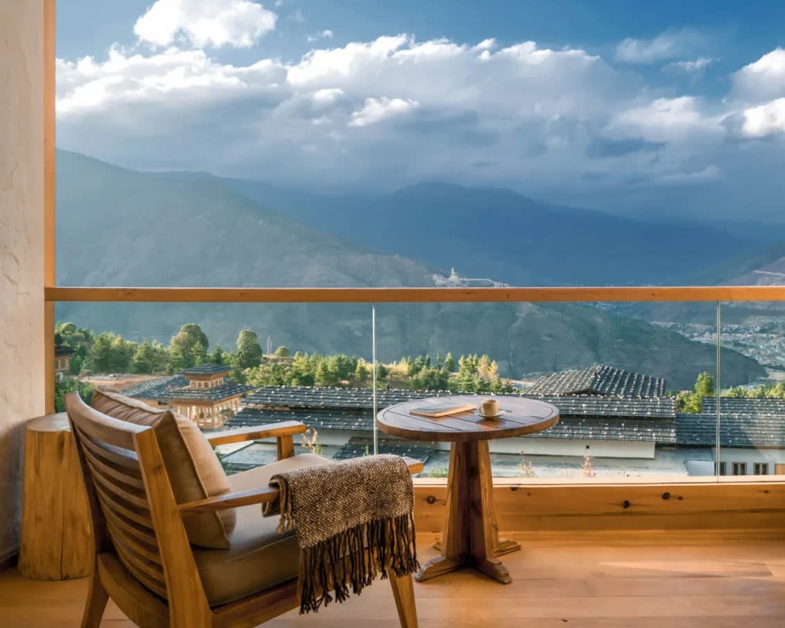 wood chair with blanket on glass lined balcony overlooking cloud covered hills during day