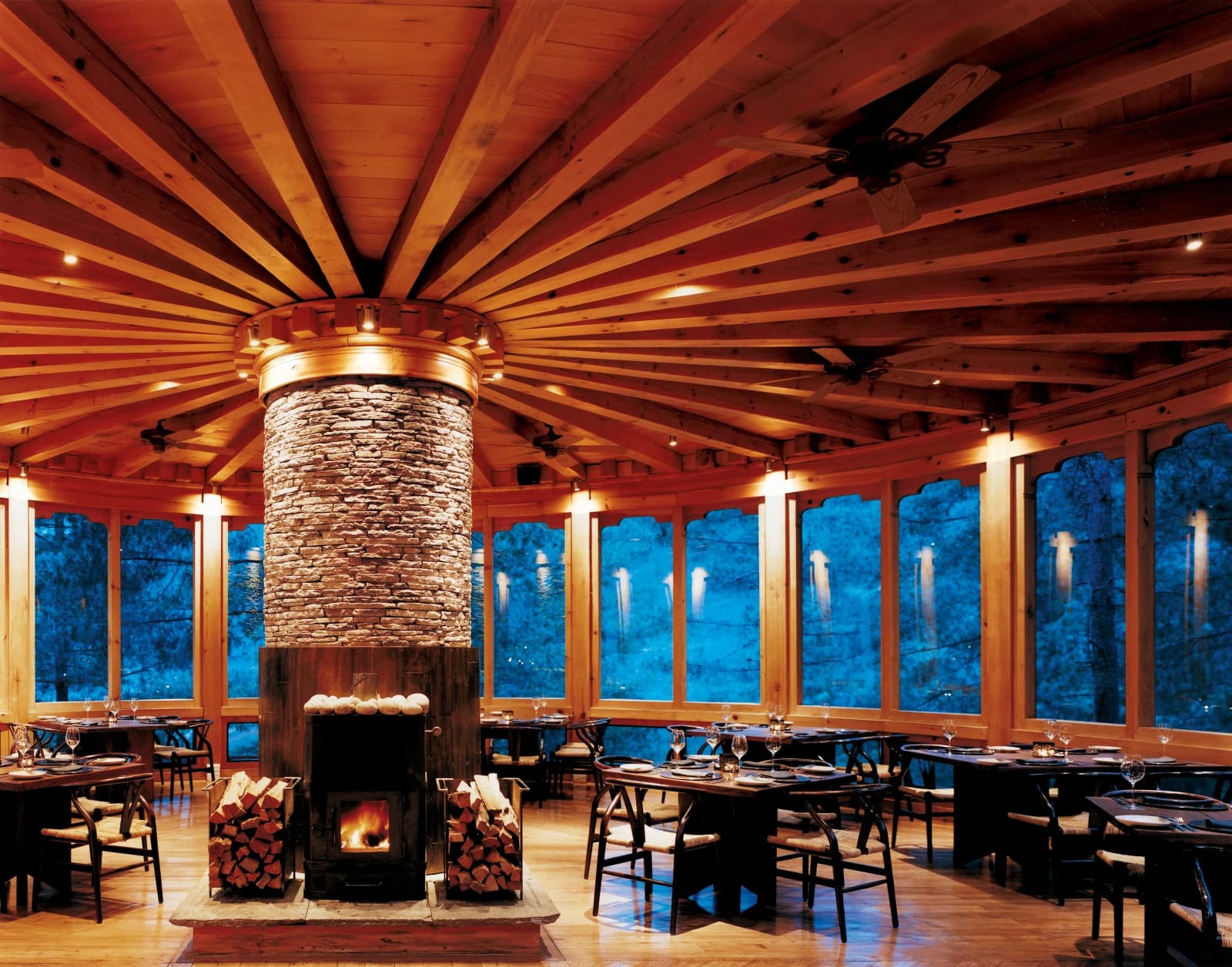 tables and chairs in a round wooden room with windows and a stone fireplace at the center
