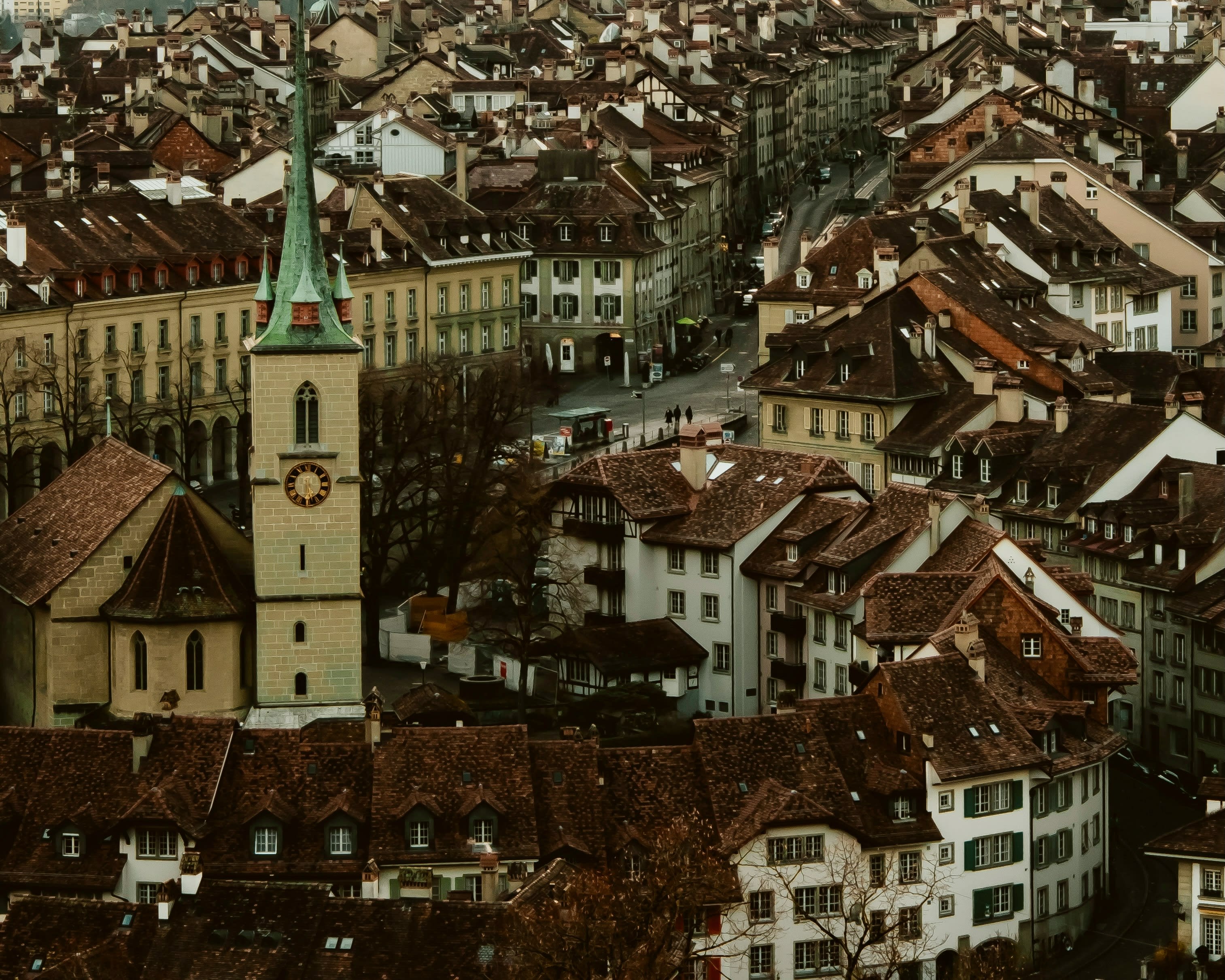 cityscape of brown rooftops, white buildings and green church steeple.