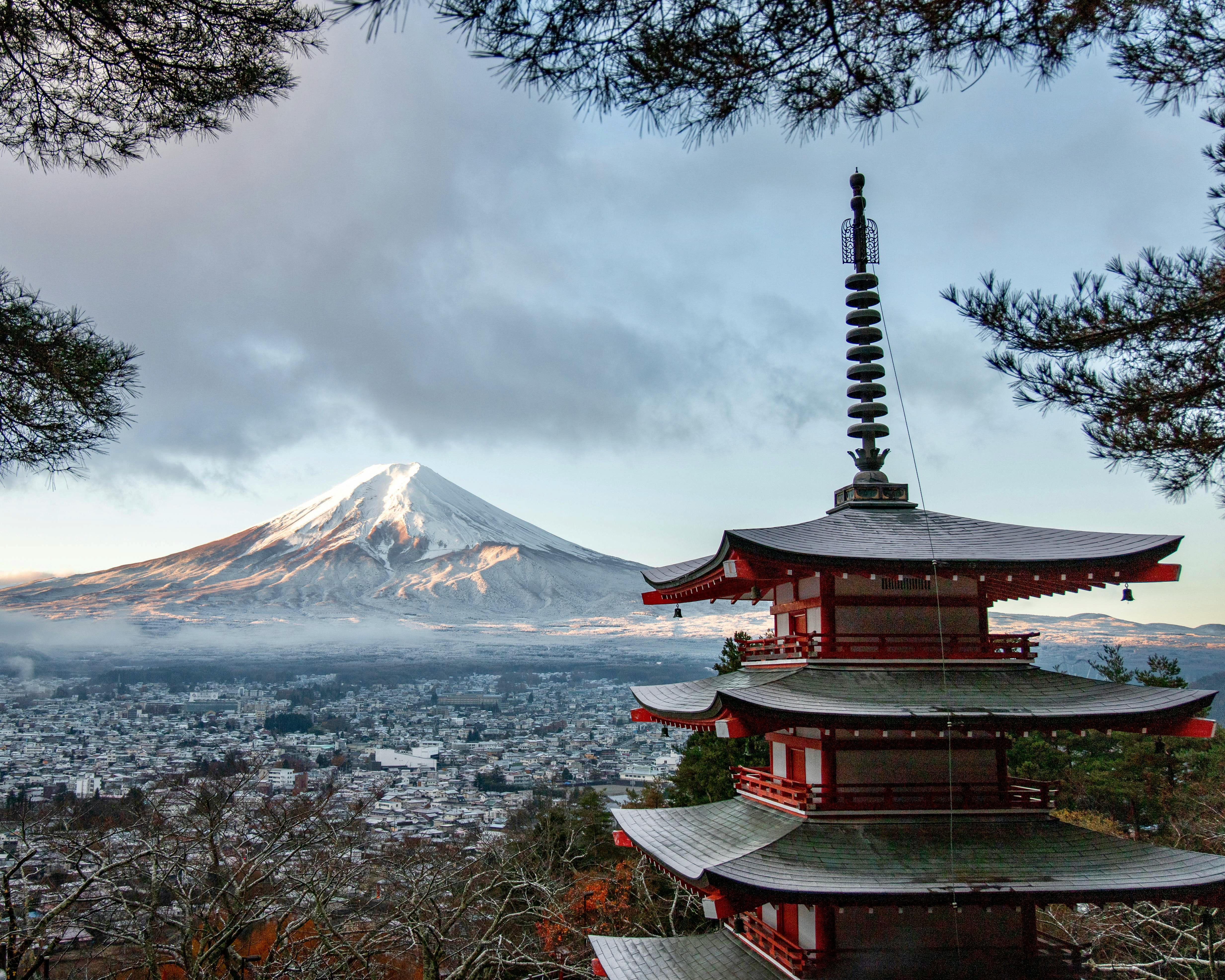 red shrine under pine trees with city and snow covered mountain in the background