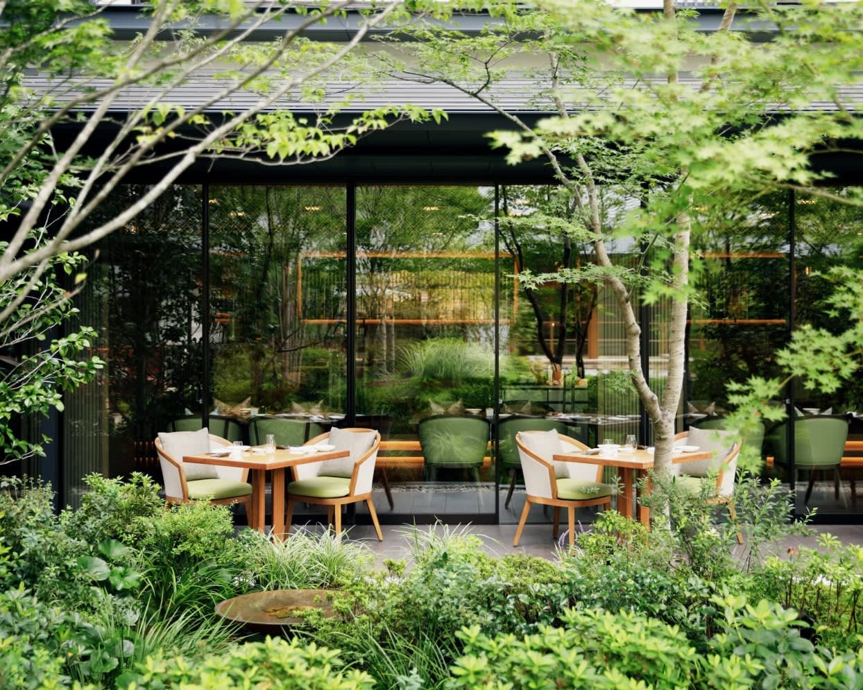 white chairs and tan tables in an outdoor green space in front of reflecting glass windows