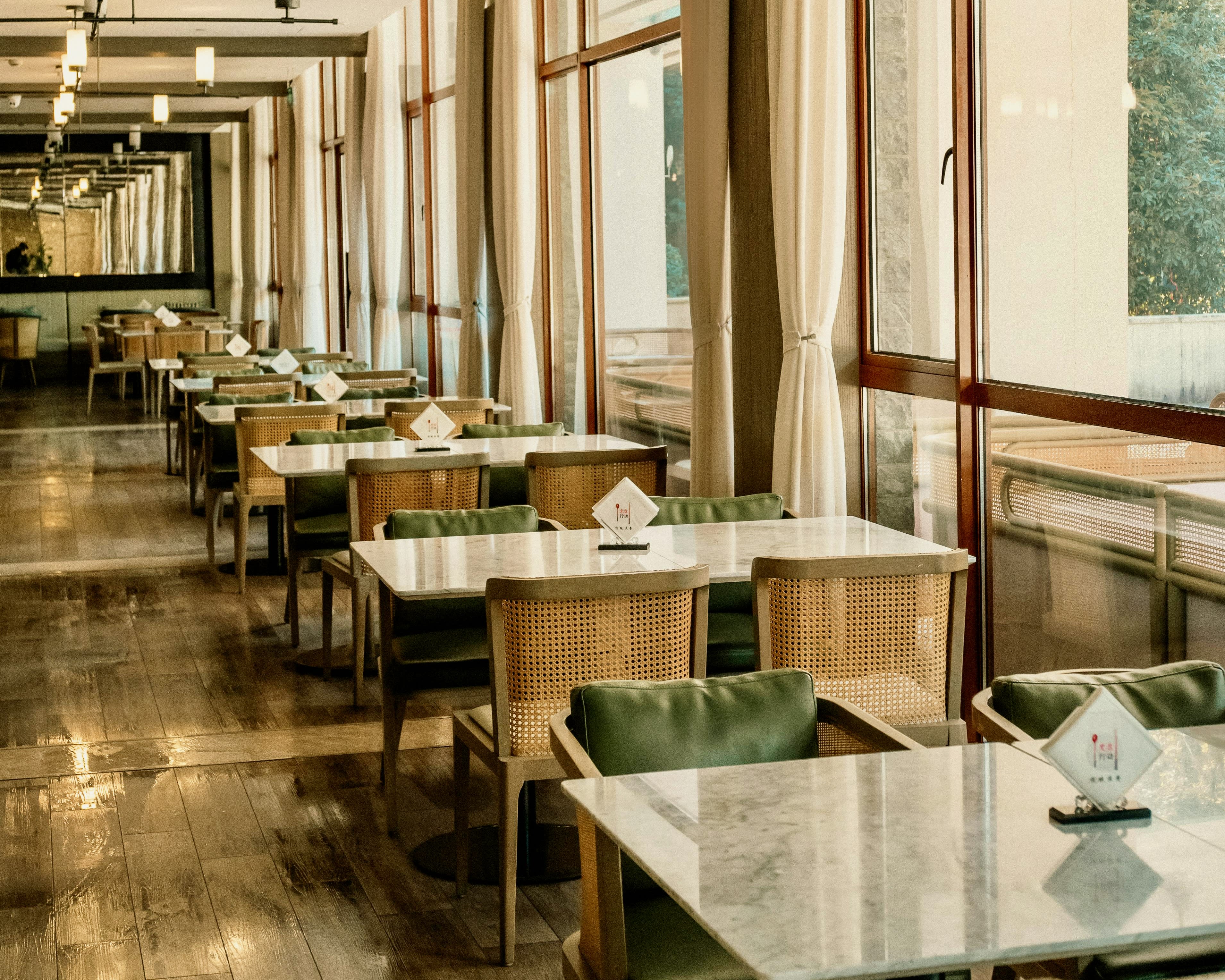 light wood chairs, green cushions, and white marble table tops in a restaurant