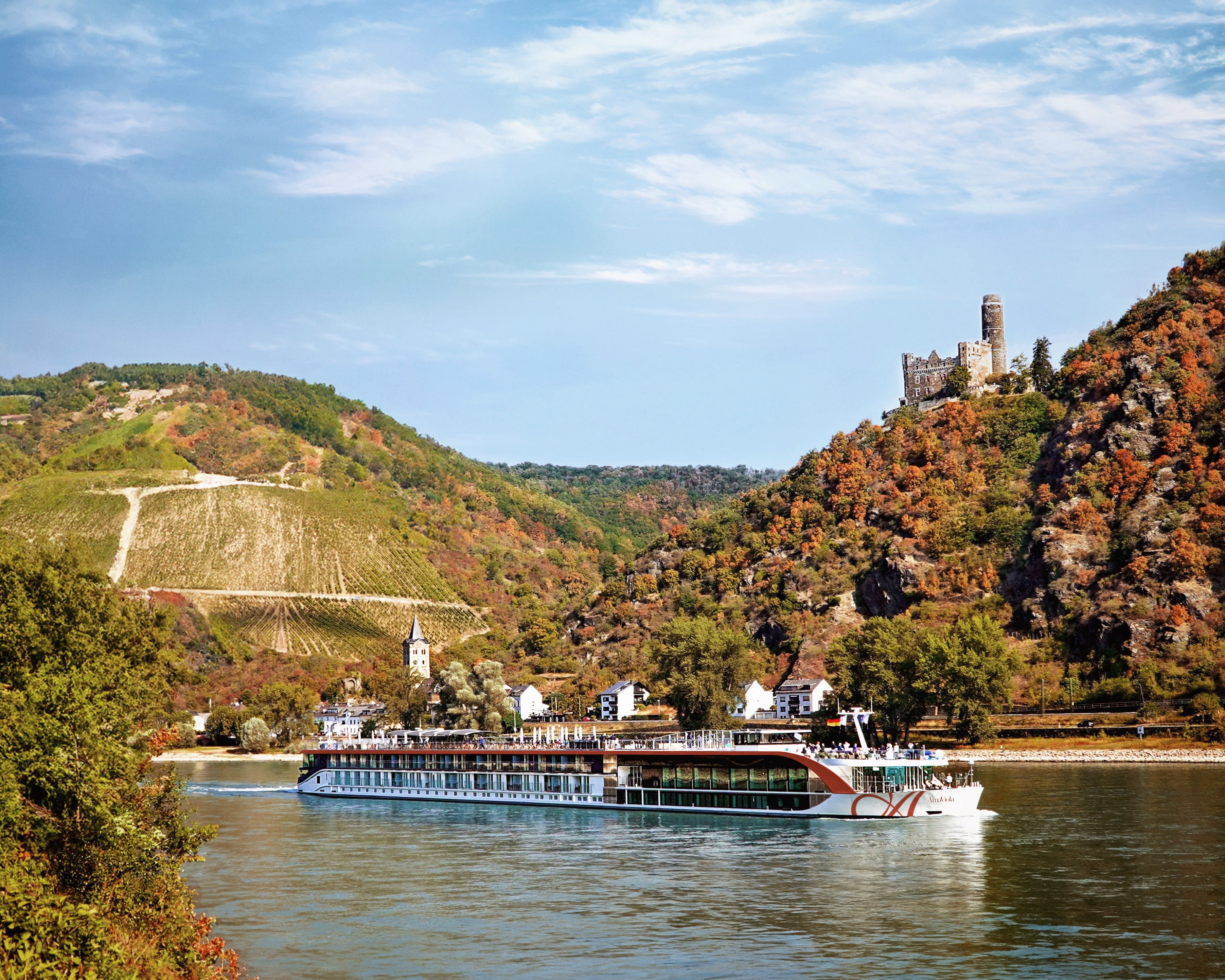 white and brown river cruise ship on a river next to a castle topped hill during day