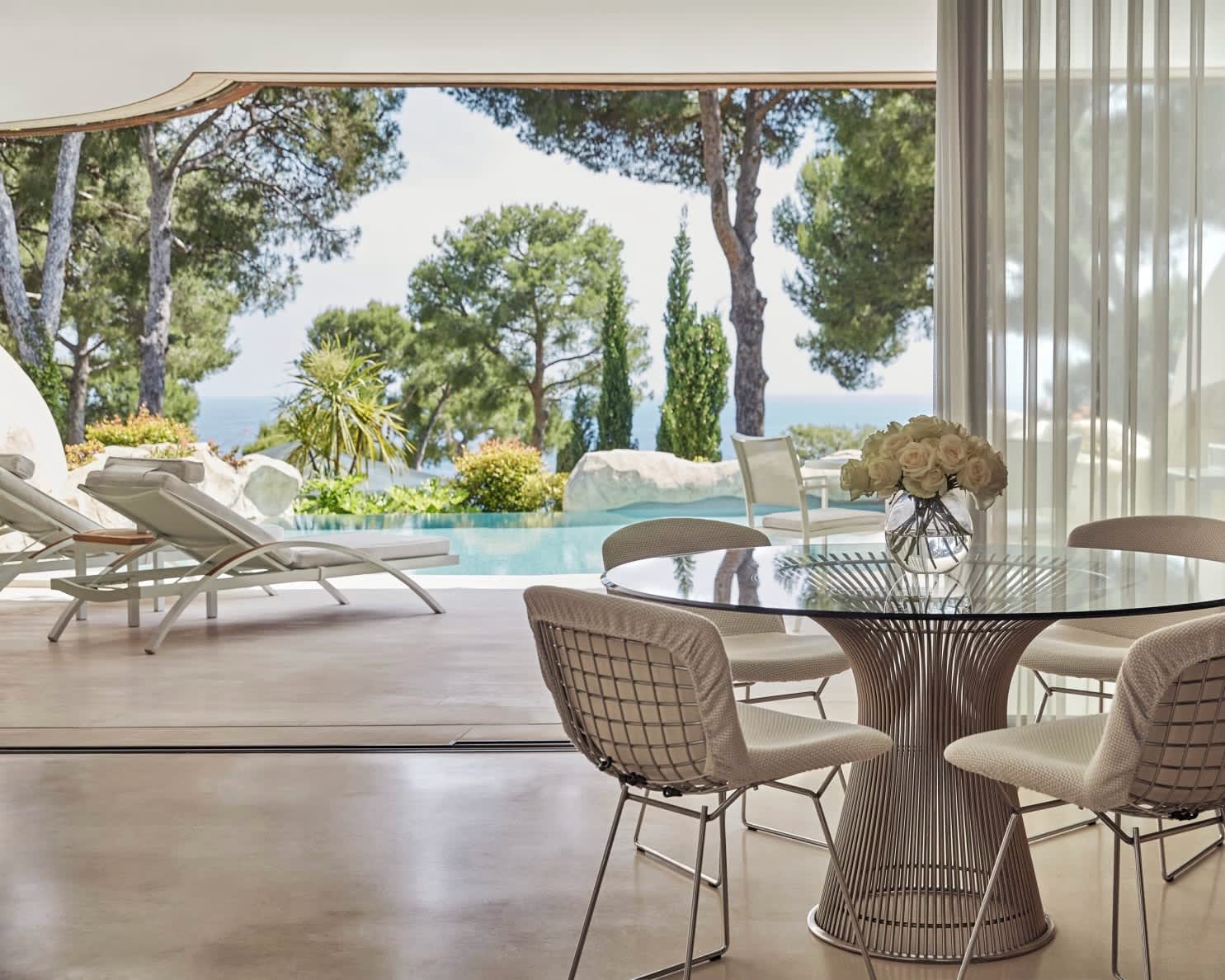 hotel room with table and chairs overlooking open terrace with lounge chairs and pool beyond