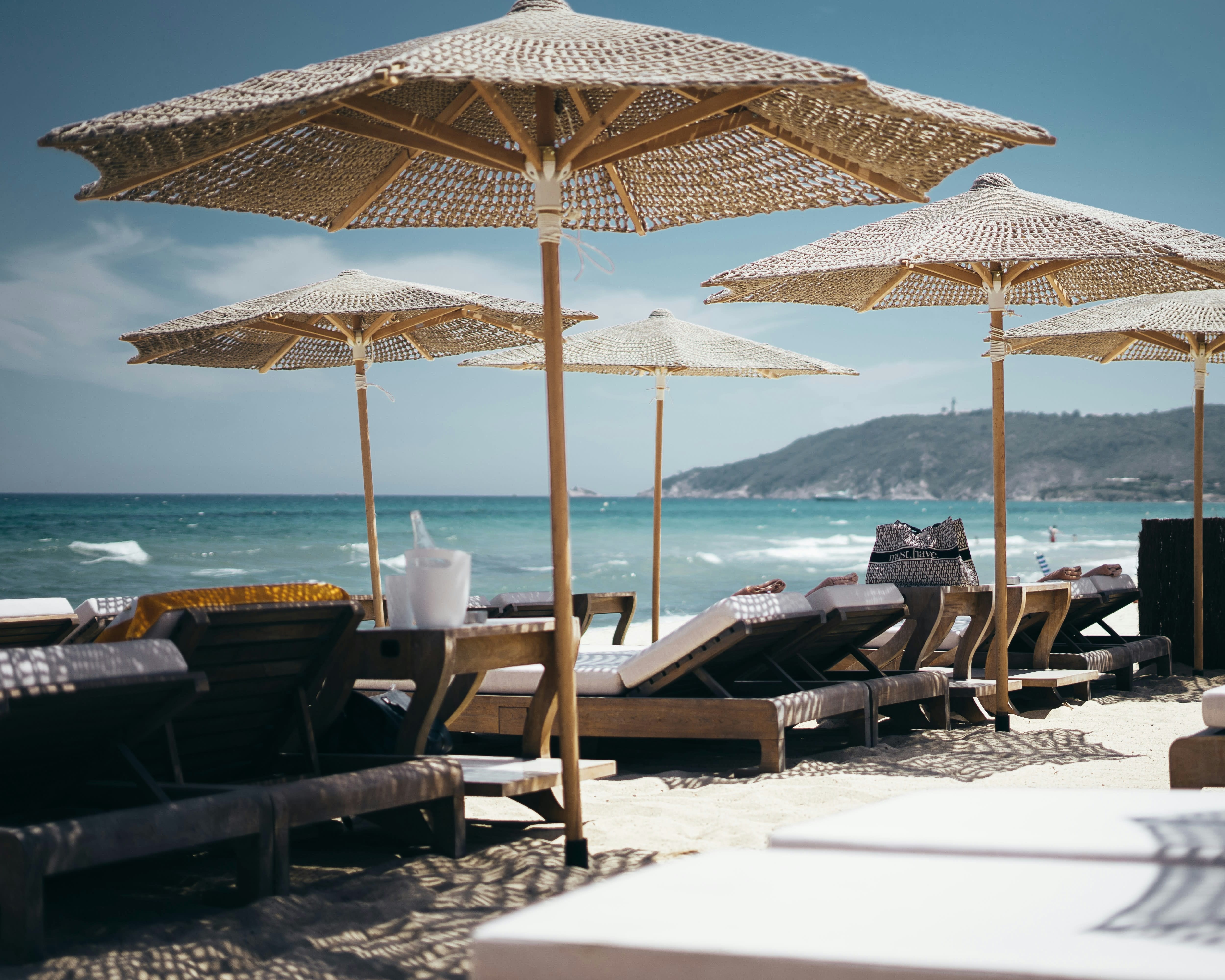 tan umbrellas over wood beach loungers in white sand at a beach club with turquoise water off shore