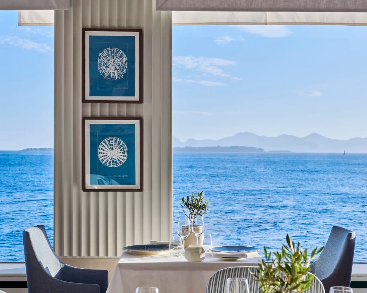 modern dining table and chairs next to tall windows overlooking blue ocean waves